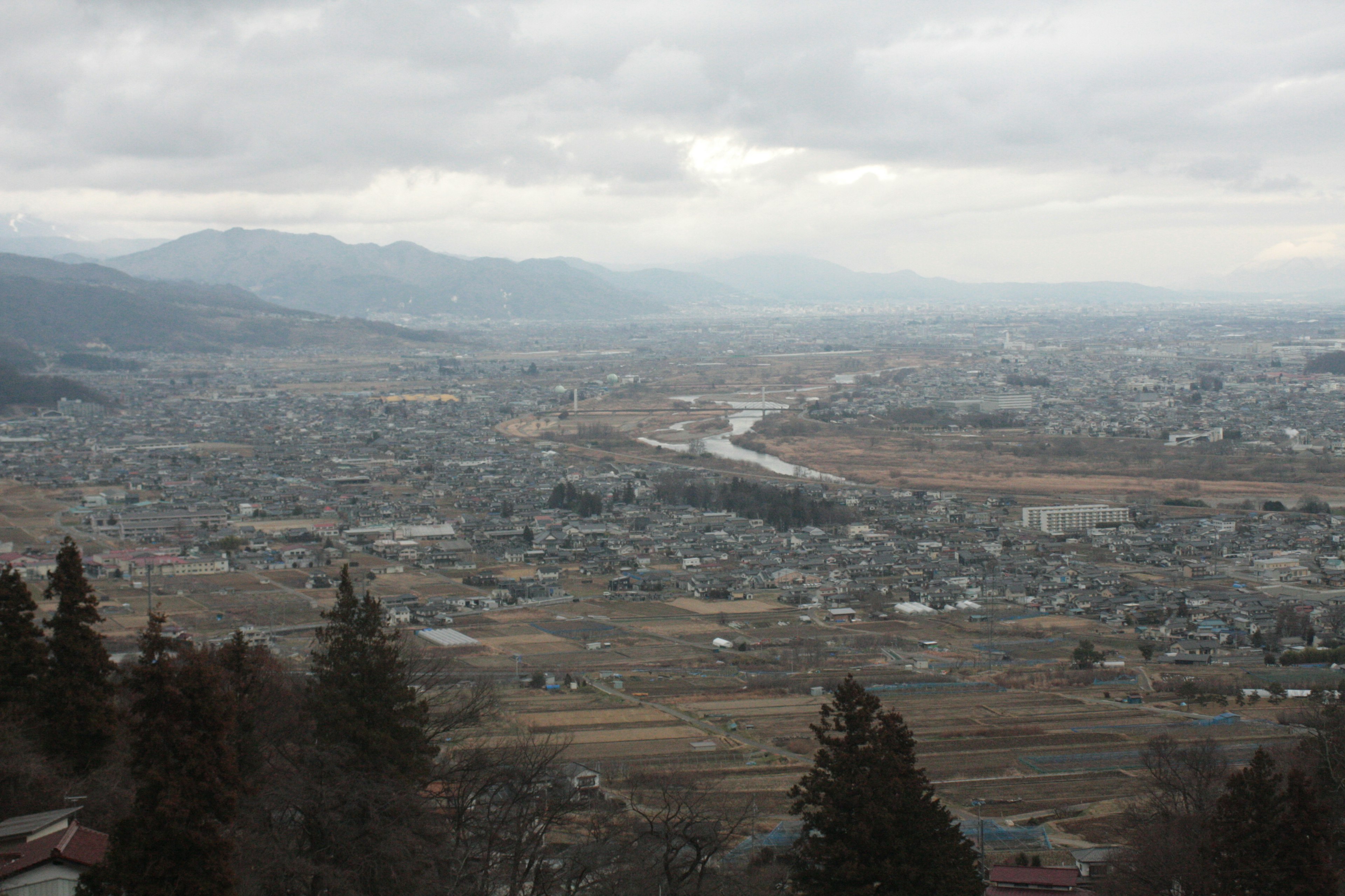 Scenic view of a quiet town surrounded by mountains overcast sky and a gentle river flowing