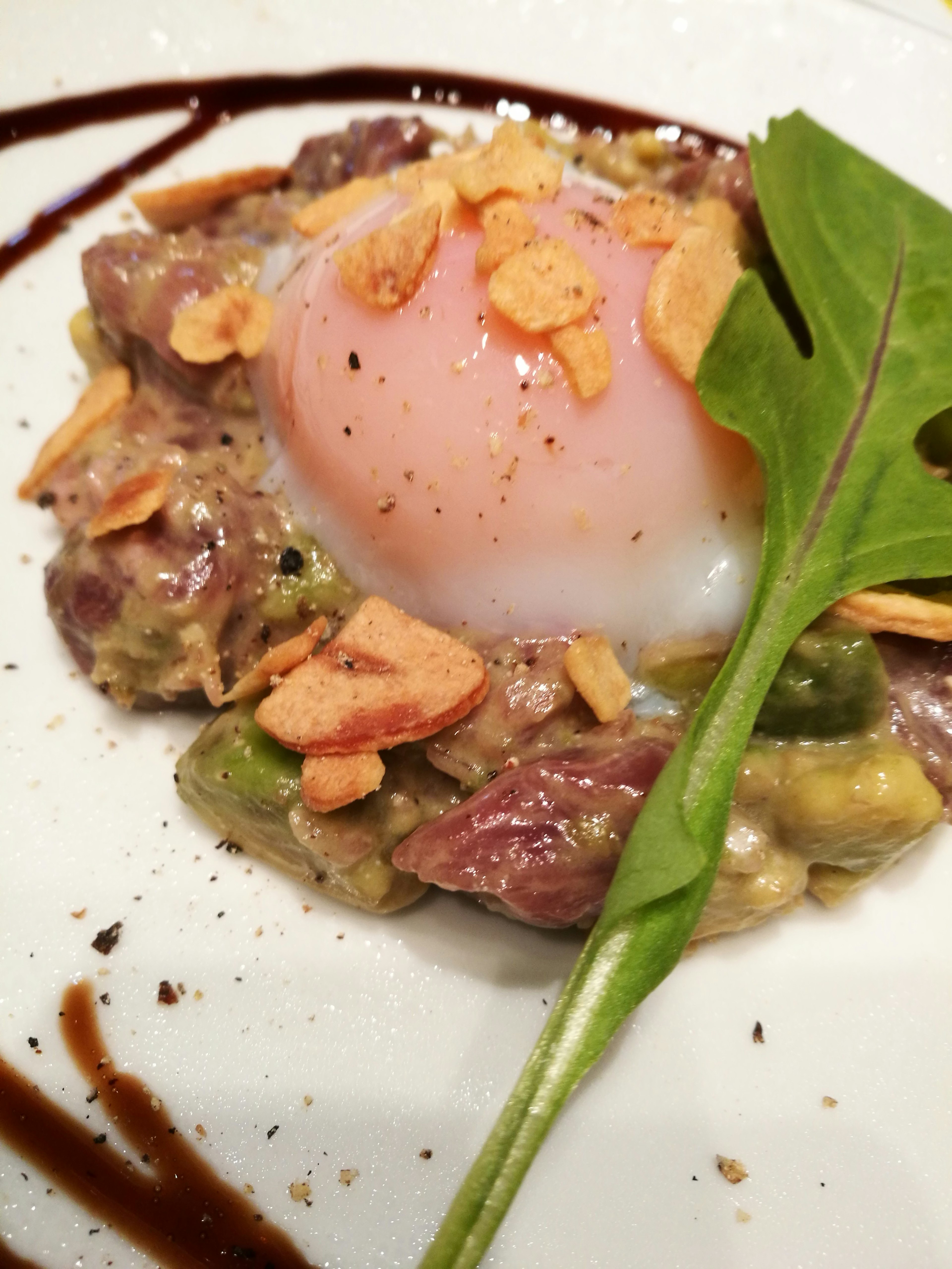 Un plato con salsa cremosa, carne y un huevo poche cubierto con almendras y verduras