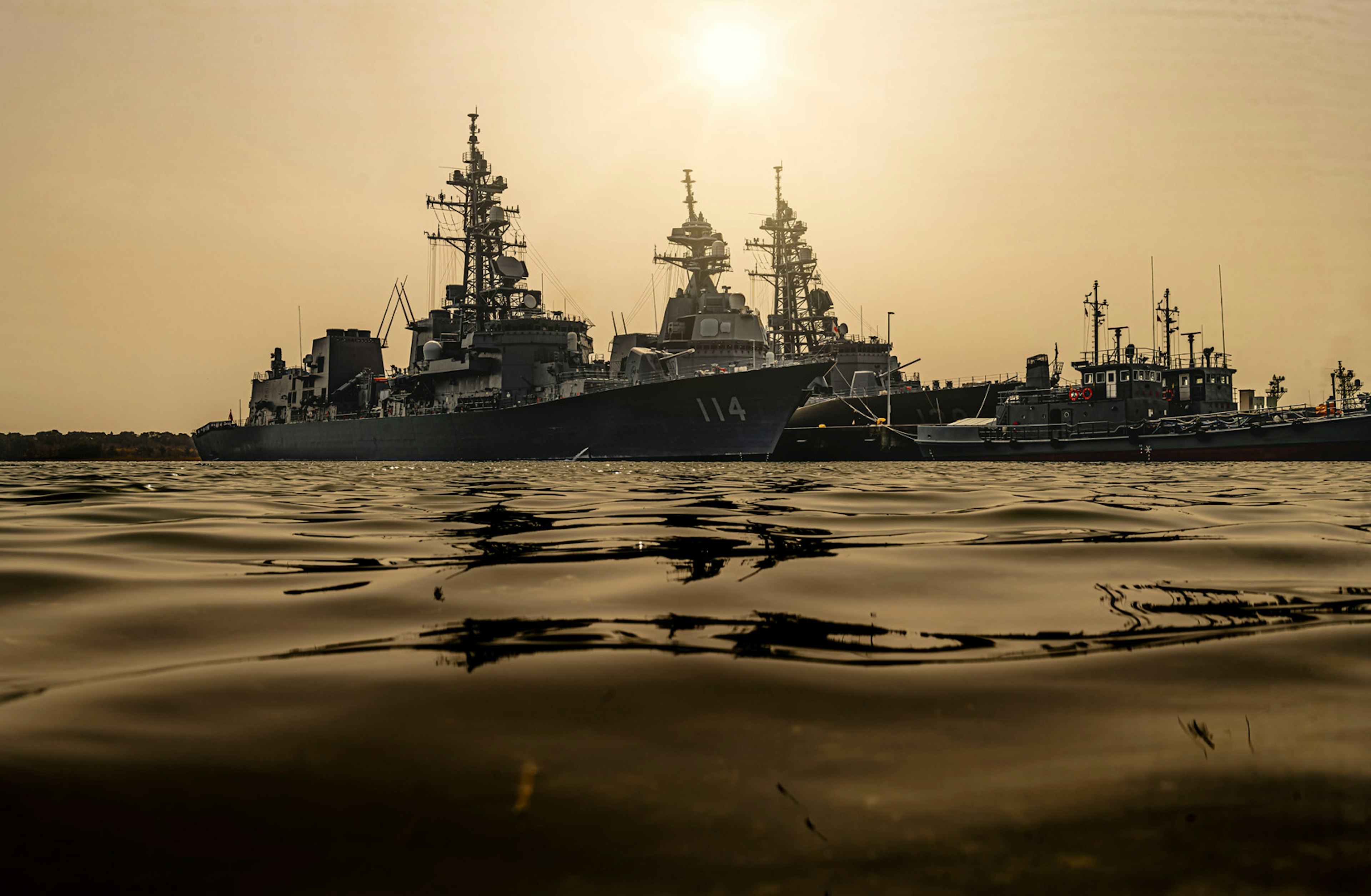 Naval ships silhouetted against a sunset over the water