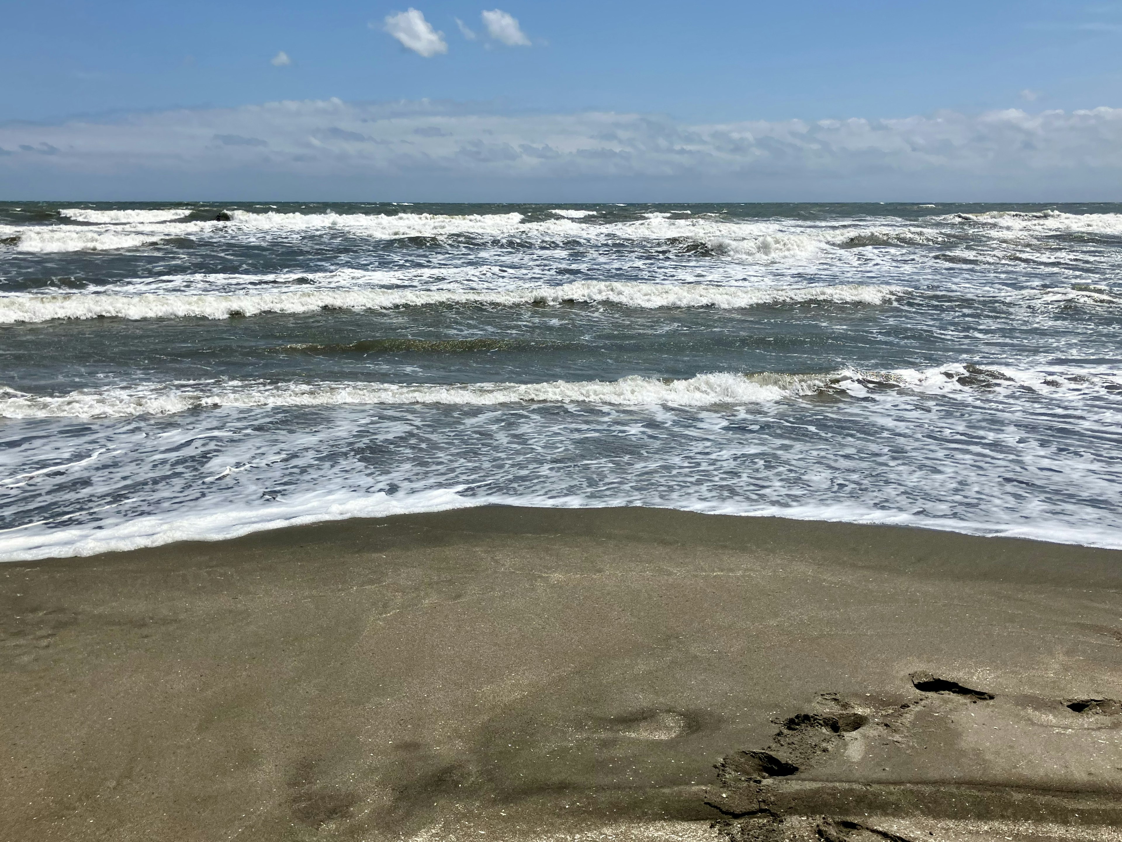 Blick auf den Ozean mit Wellen sandstrand fußabdrücke blauer himmel und weiße wolken