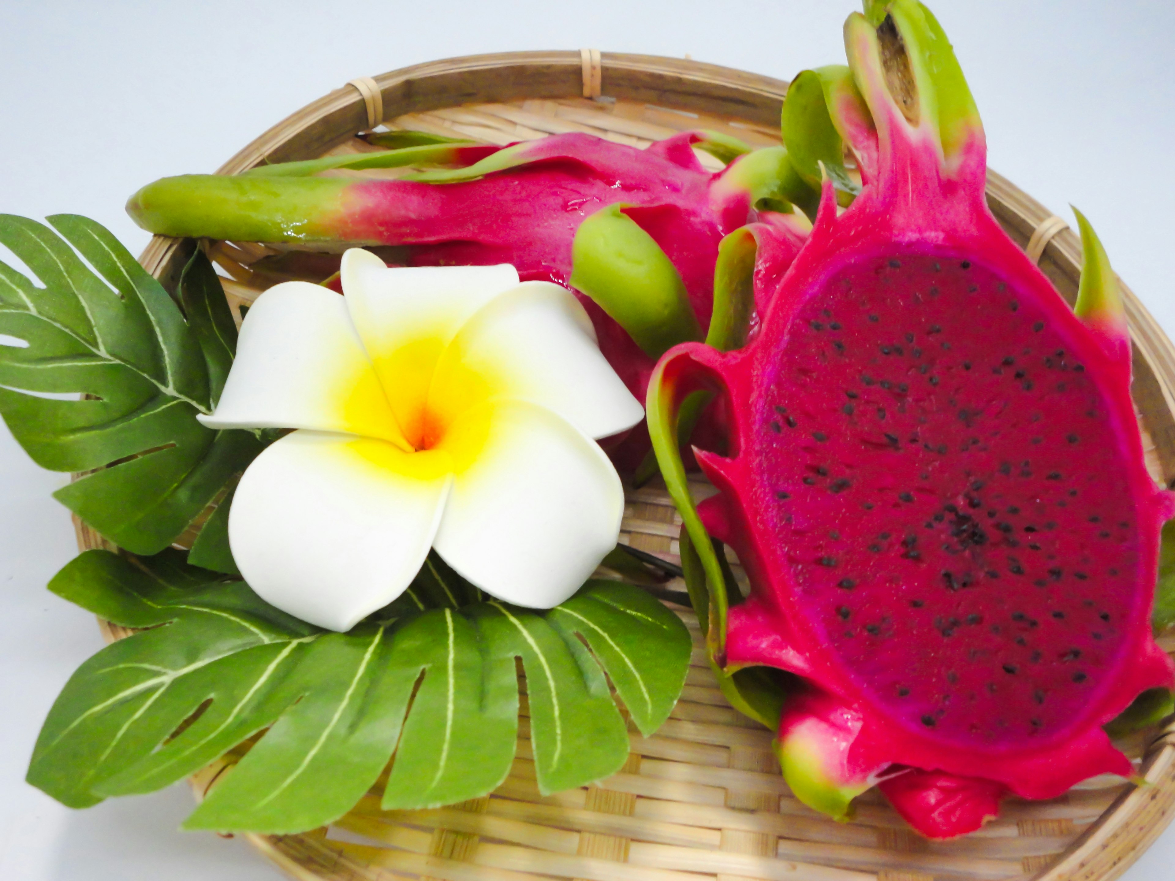 Colorful dragon fruit and white plumeria flower arranged in a basket