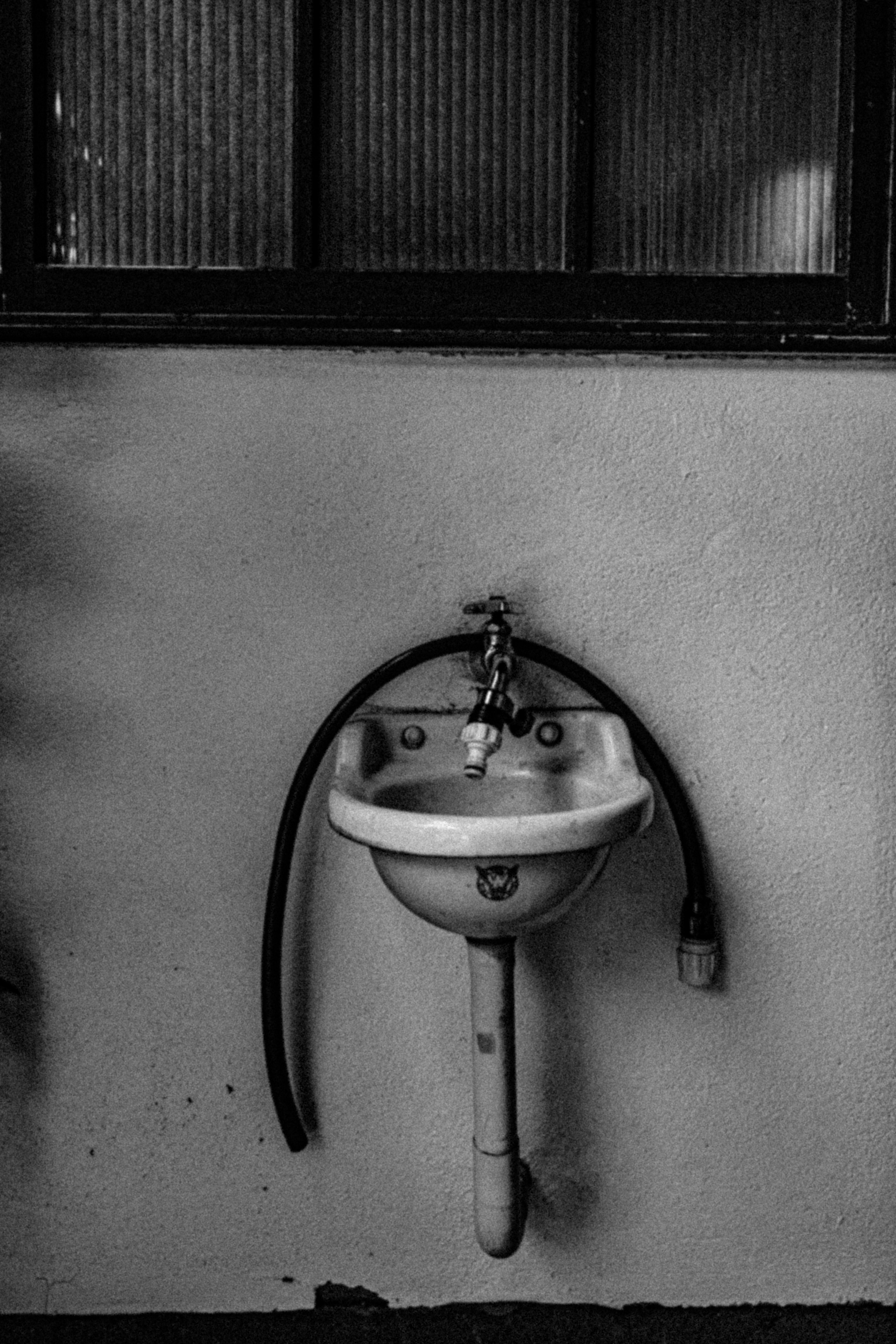 Old white sink mounted on the wall with a black hose