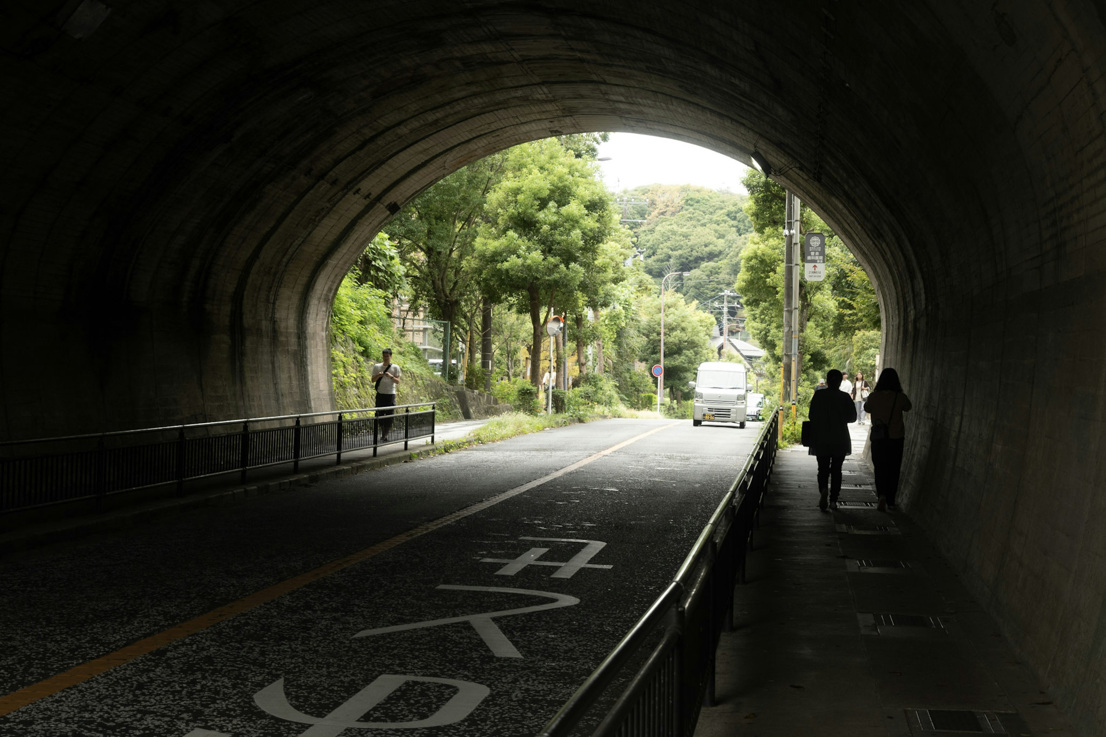 トンネルの中から見た道と人々のシルエット 緑の木々が周囲にあり