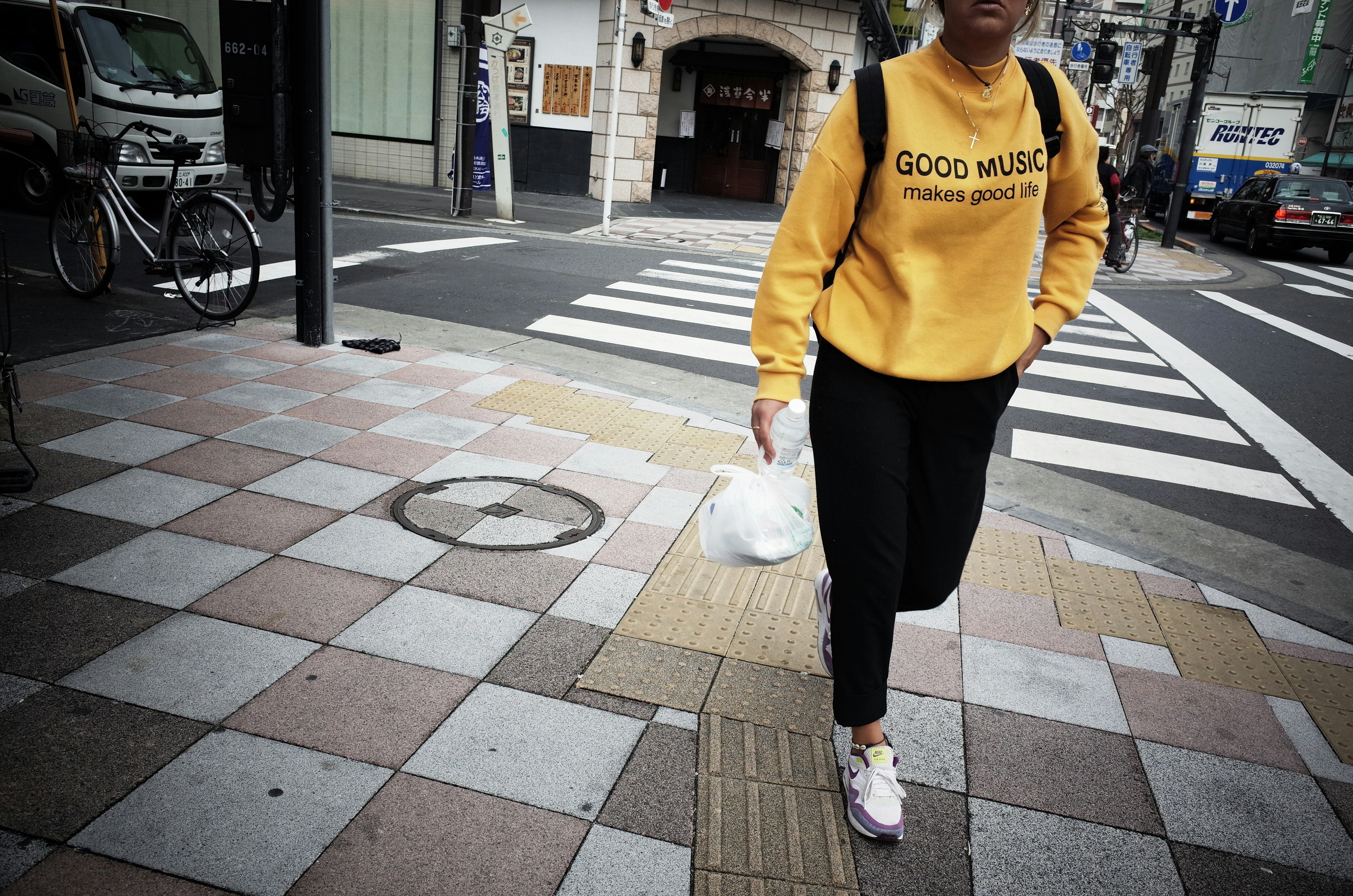 Eine Frau in einem gelben Sweatshirt, die die Straße überquert