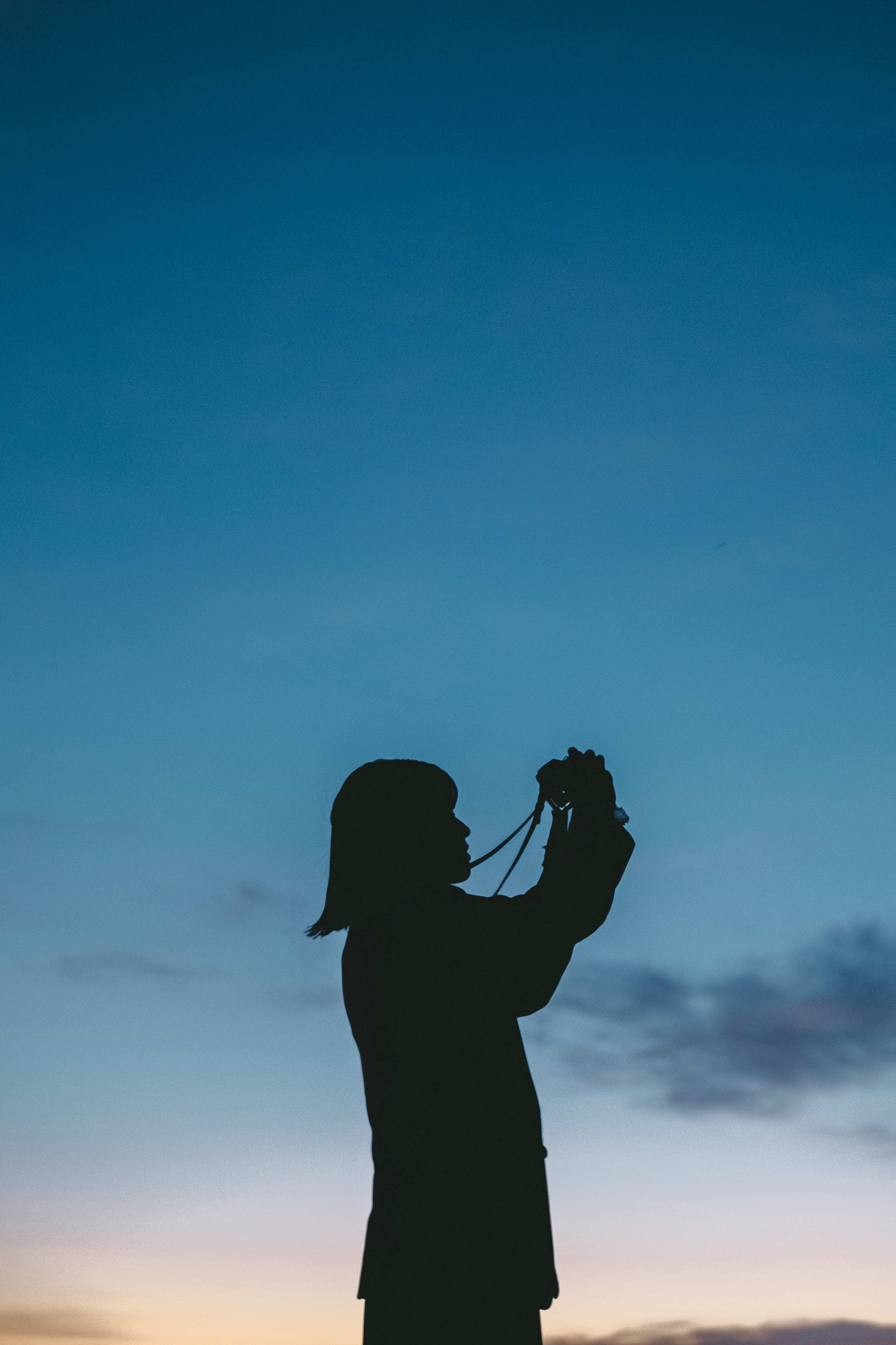 Siluet seseorang yang memegang kamera di latar belakang langit senja