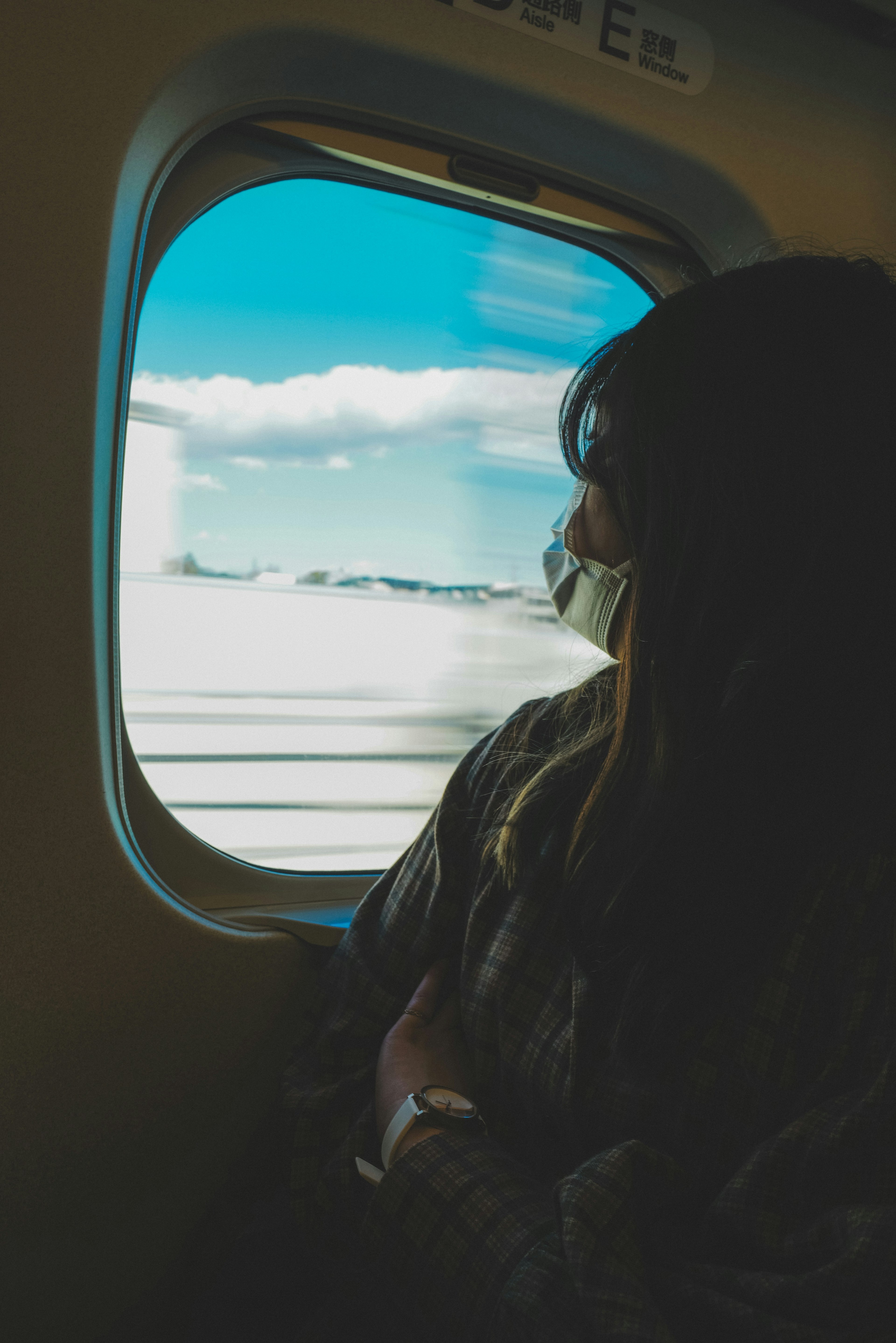 Una donna che guarda fuori da un finestrino di aereo con cielo blu e nuvole visibili