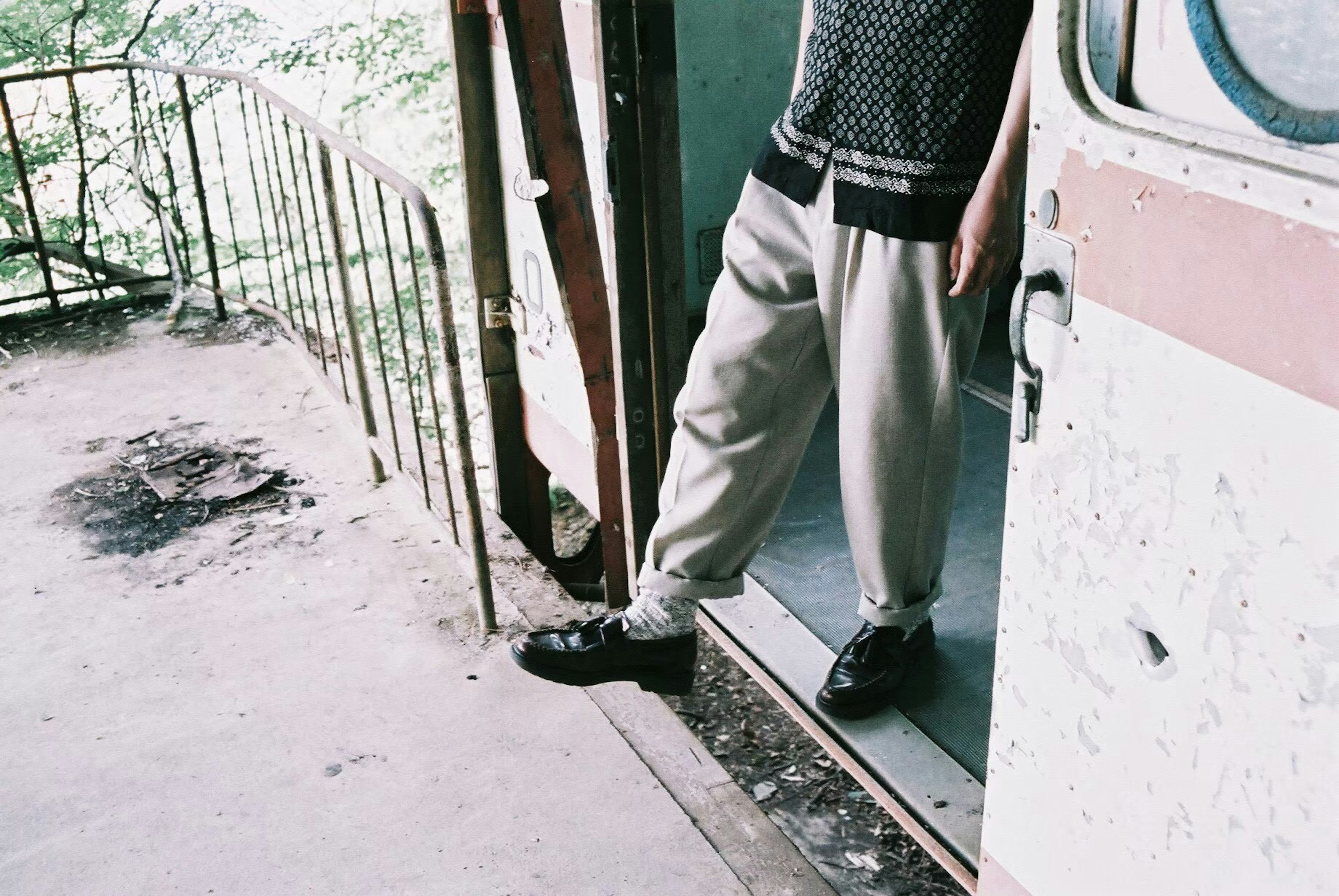 Pieds d'une personne debout à la porte portant un pantalon clair et des chaussures noires ambiance vintage