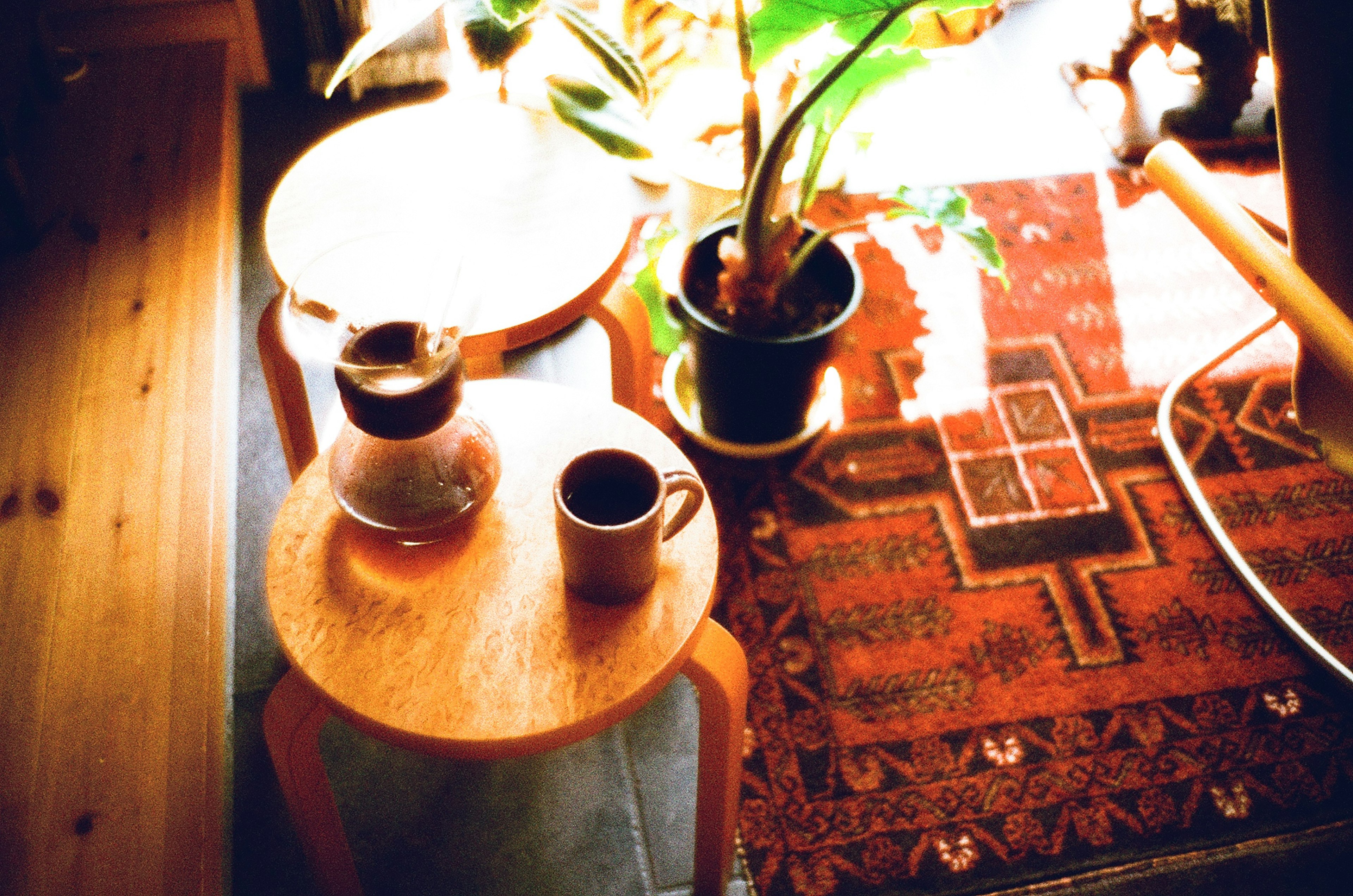 Wooden table with coffee pot and cups surrounded by a plant and a colorful rug