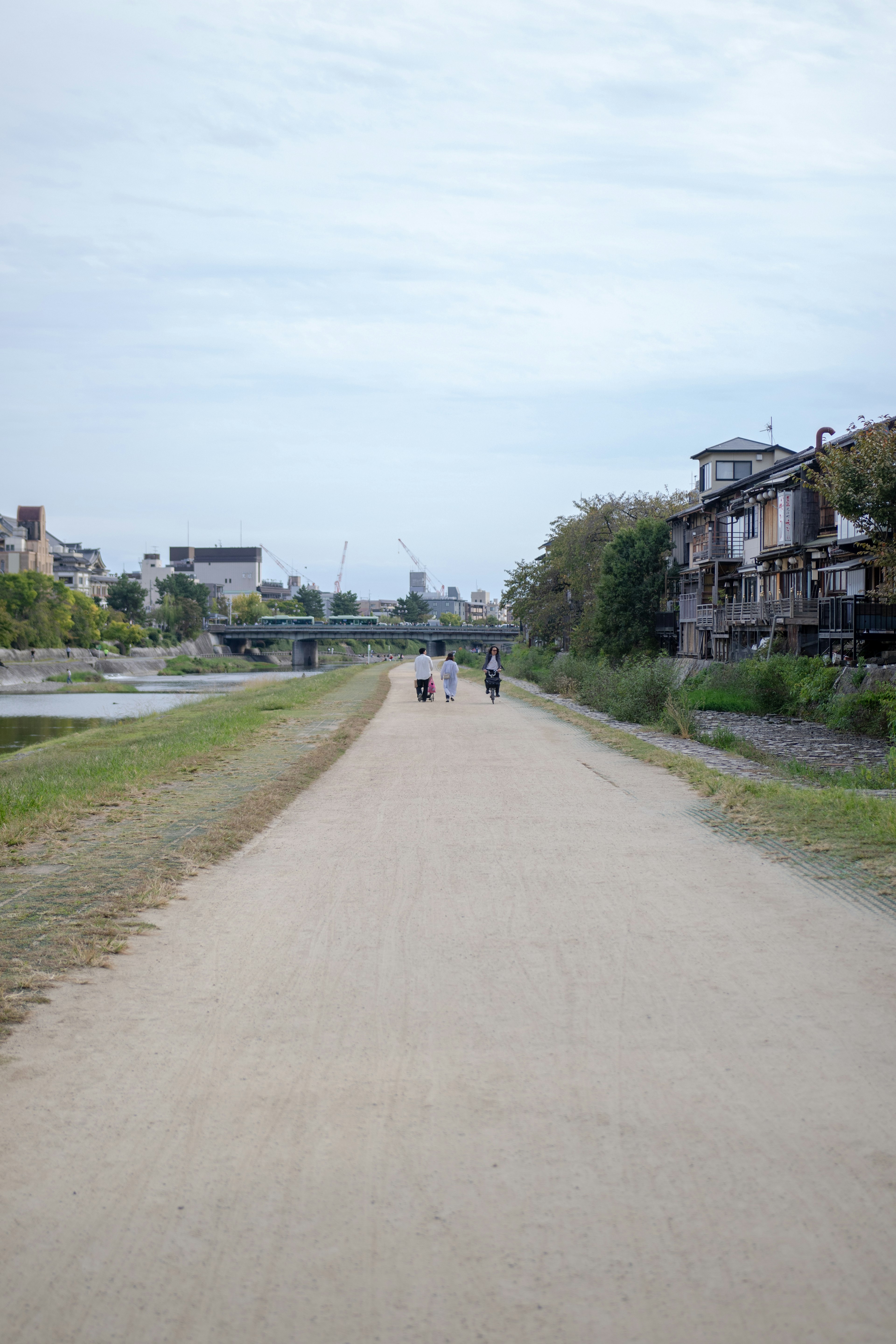 Vista escénica de un camino junto al río con personas caminando y edificios al fondo