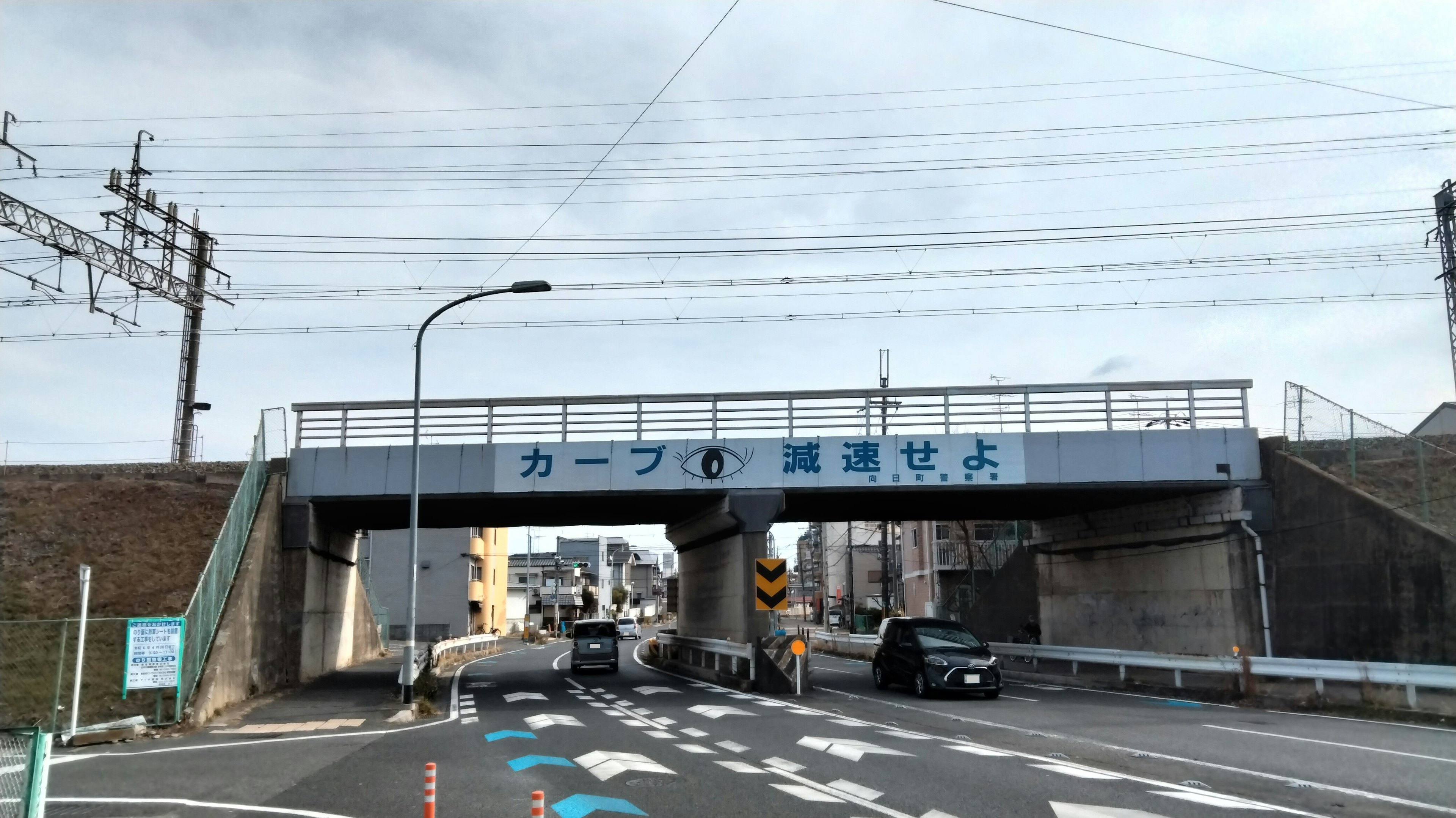 Road scene featuring a curved sign and a railway overpass