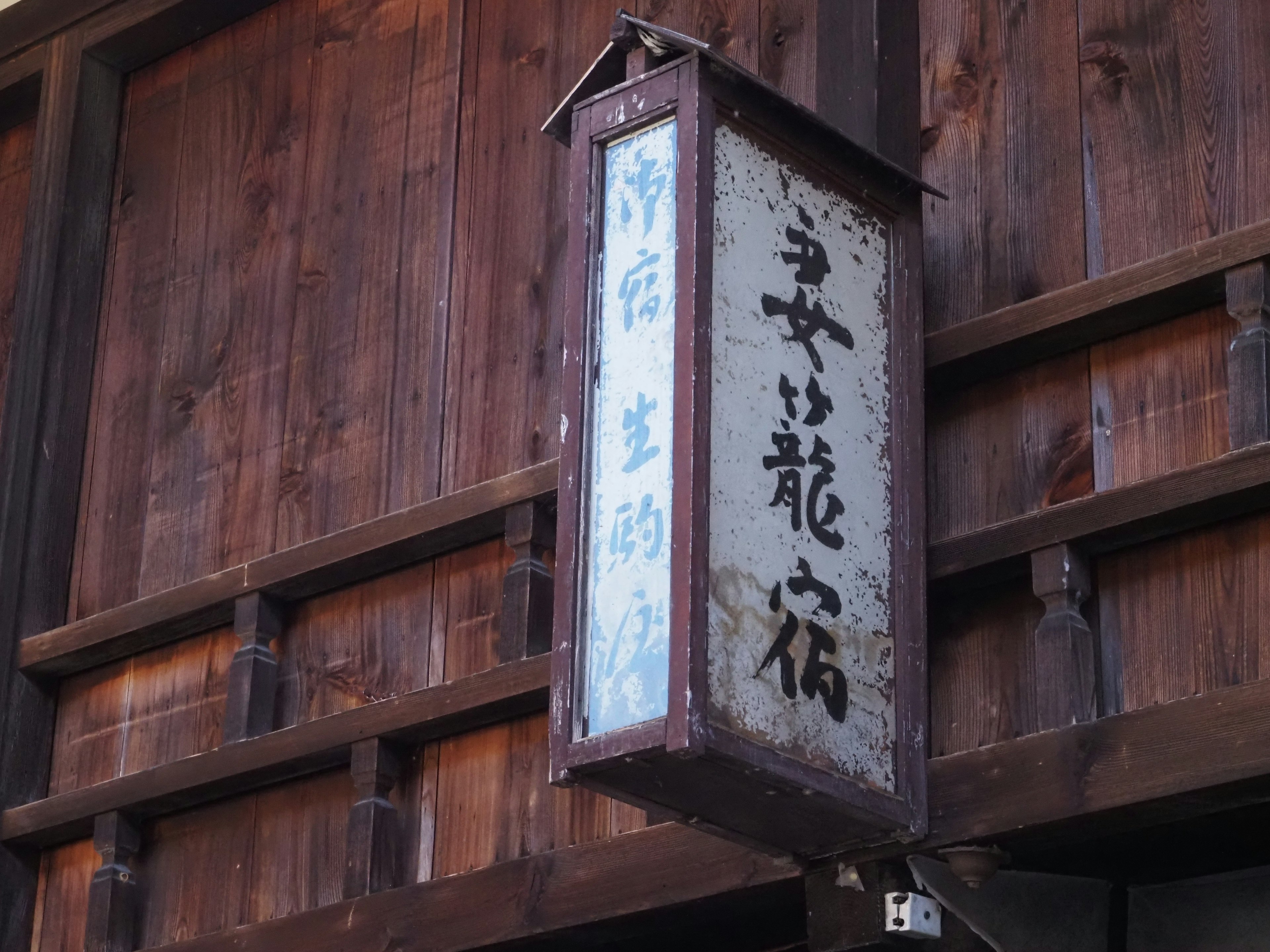 Traditional sign hanging from an old wooden building featuring Japanese text and a dragon illustration