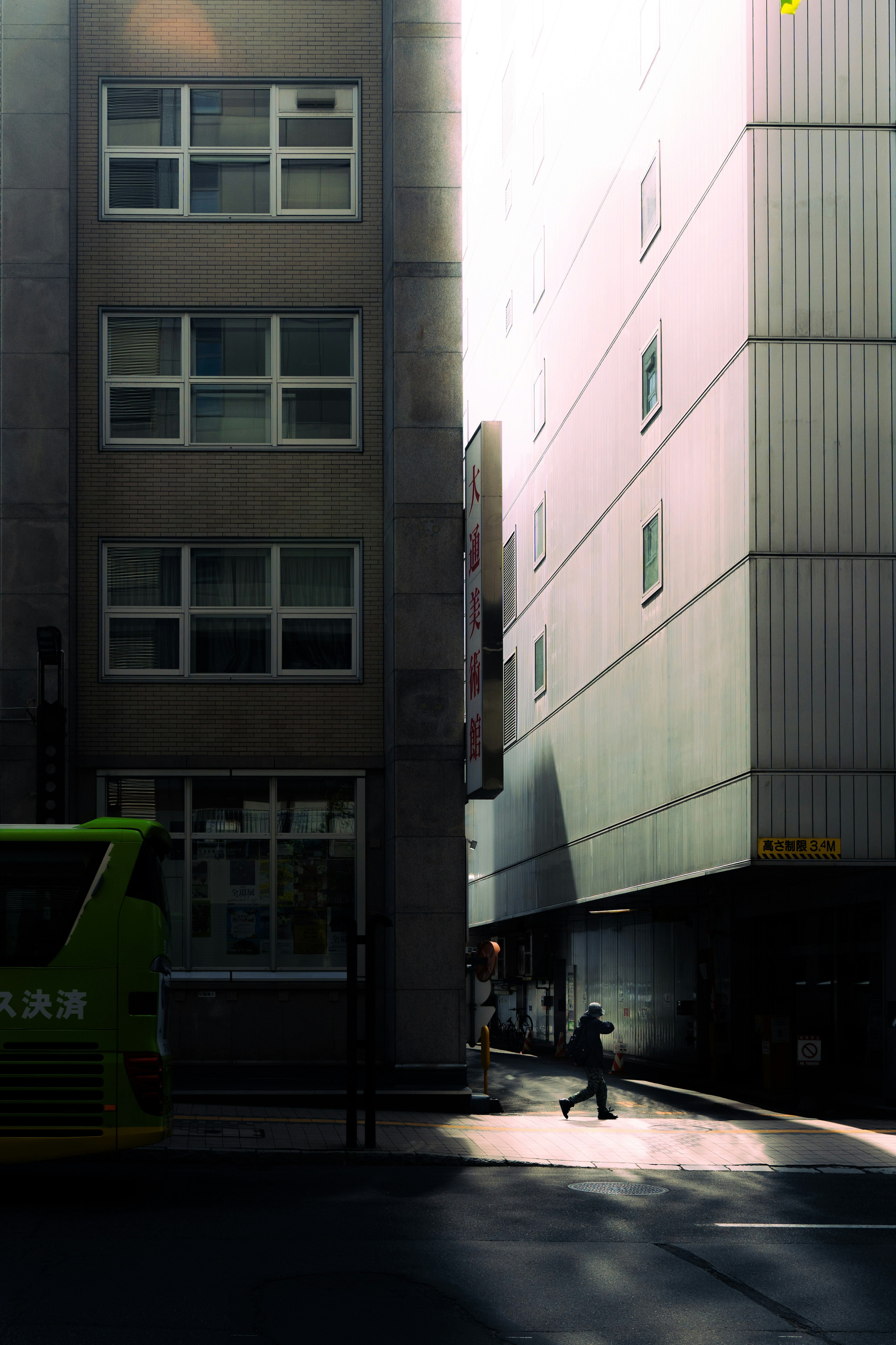 Narrow street with buildings and a green bus in the sunlight