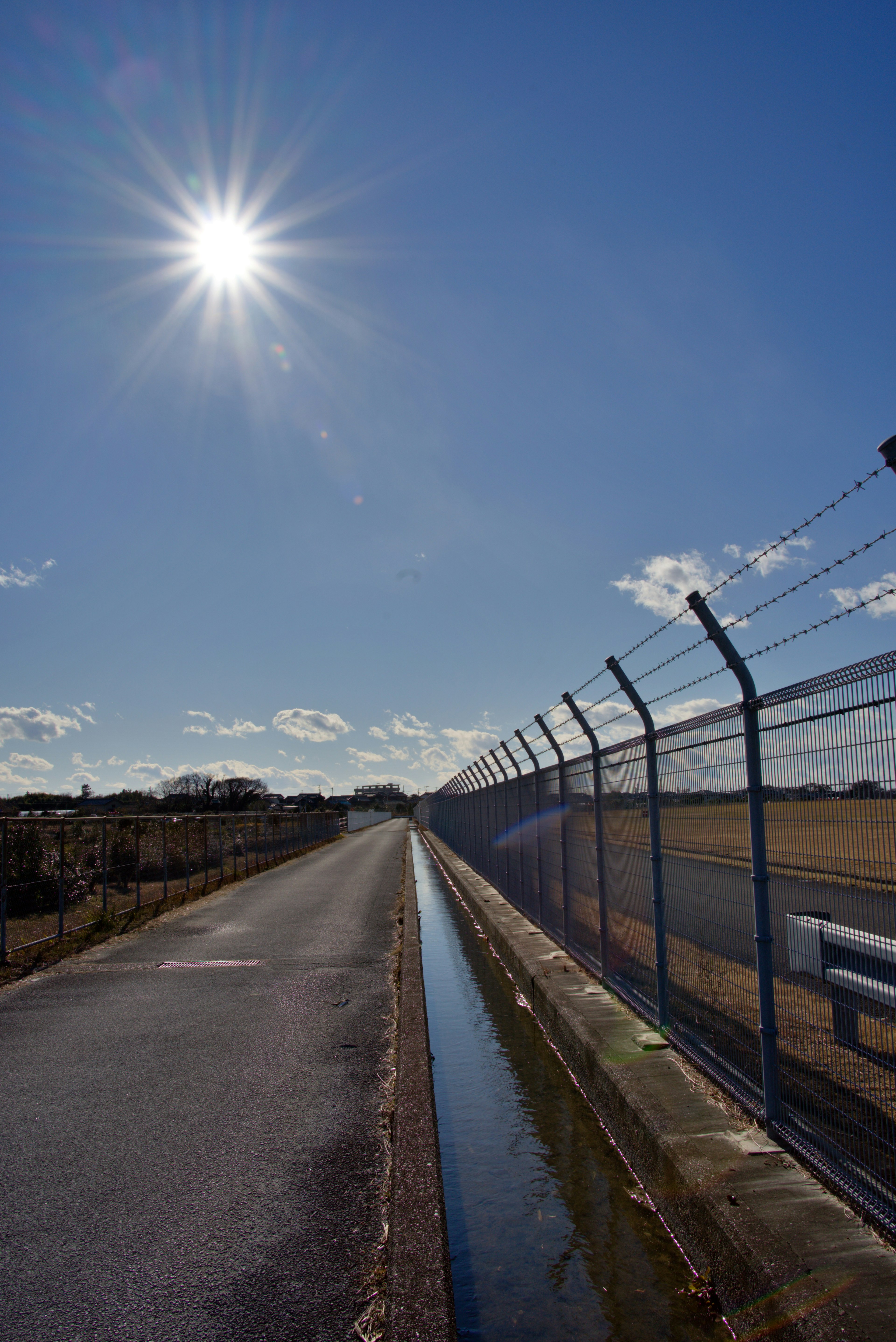 青空の下に広がる舗装された道路とフェンス 明るい太陽が輝く