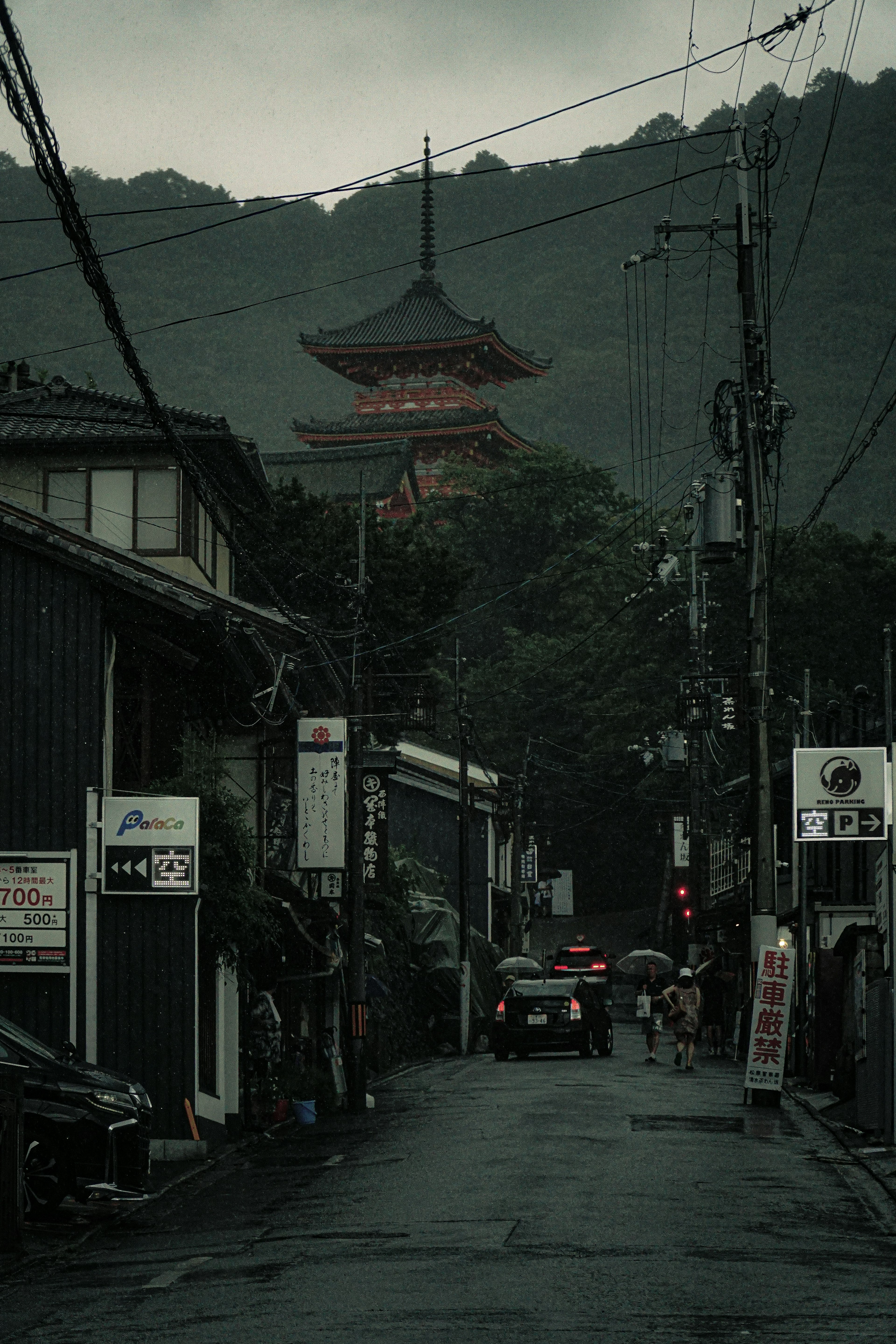 Escena de calle tranquila bajo la lluvia con una pagoda roja a lo lejos