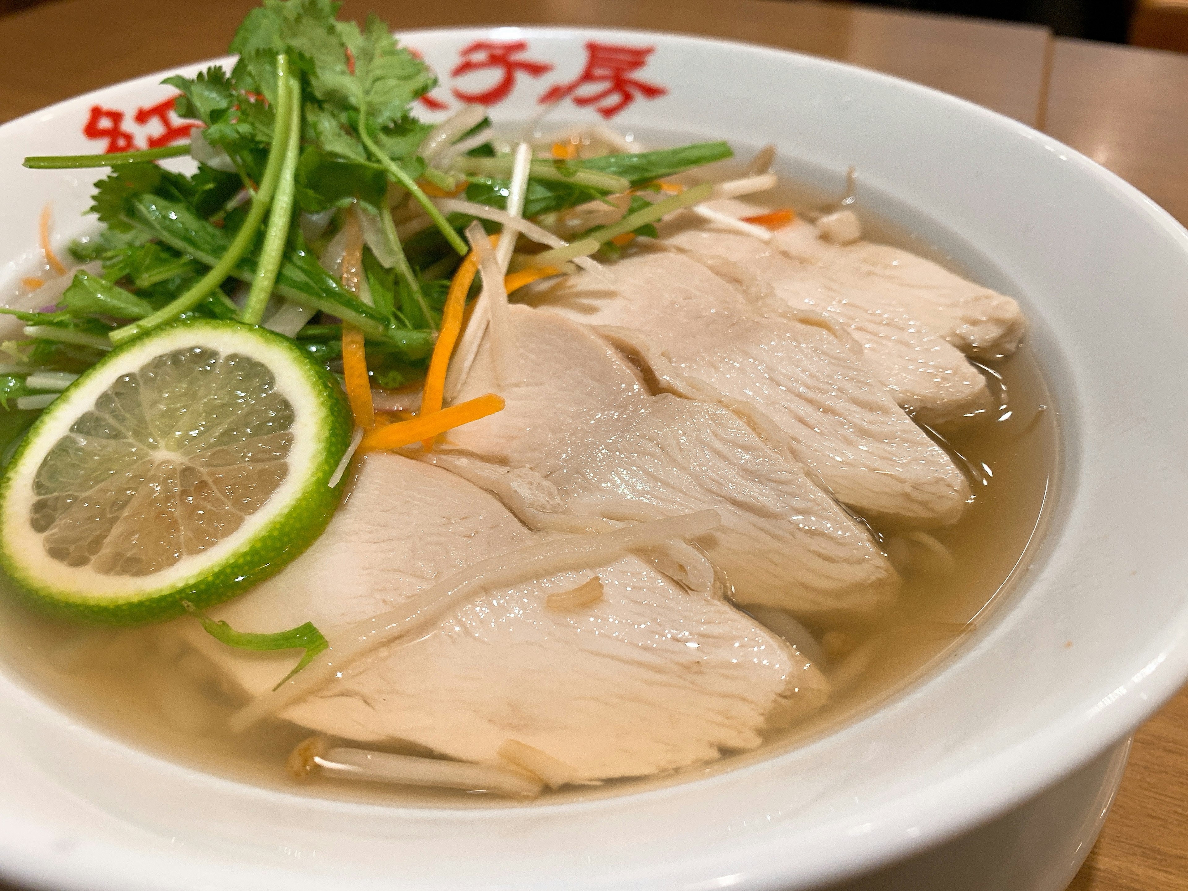 Bowl of chicken soup with sliced chicken and herbs garnished with lime