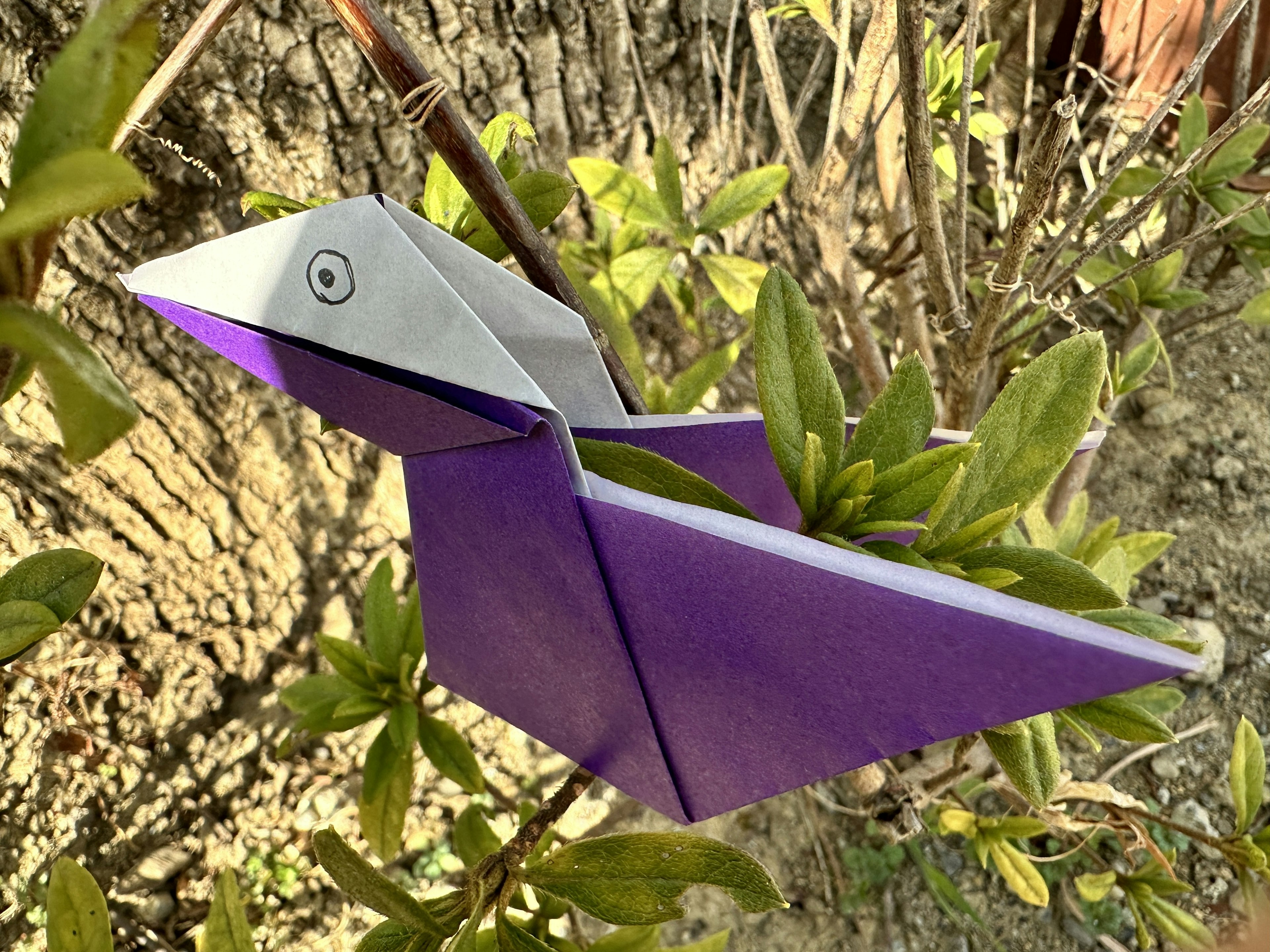 Một con chim origami màu tím đậu trên cành cây