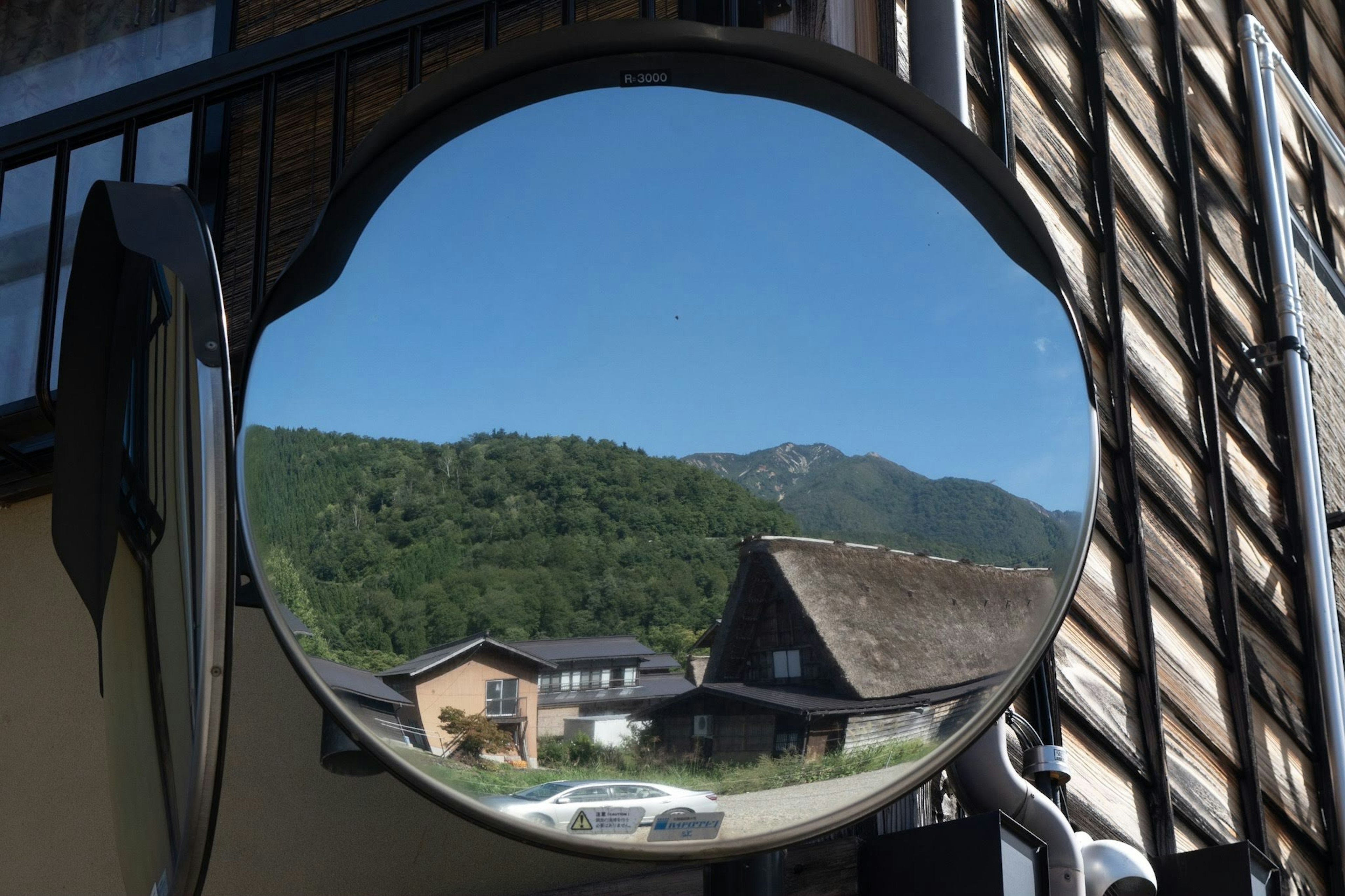 Round mirror reflecting blue sky and mountains nearby houses visible