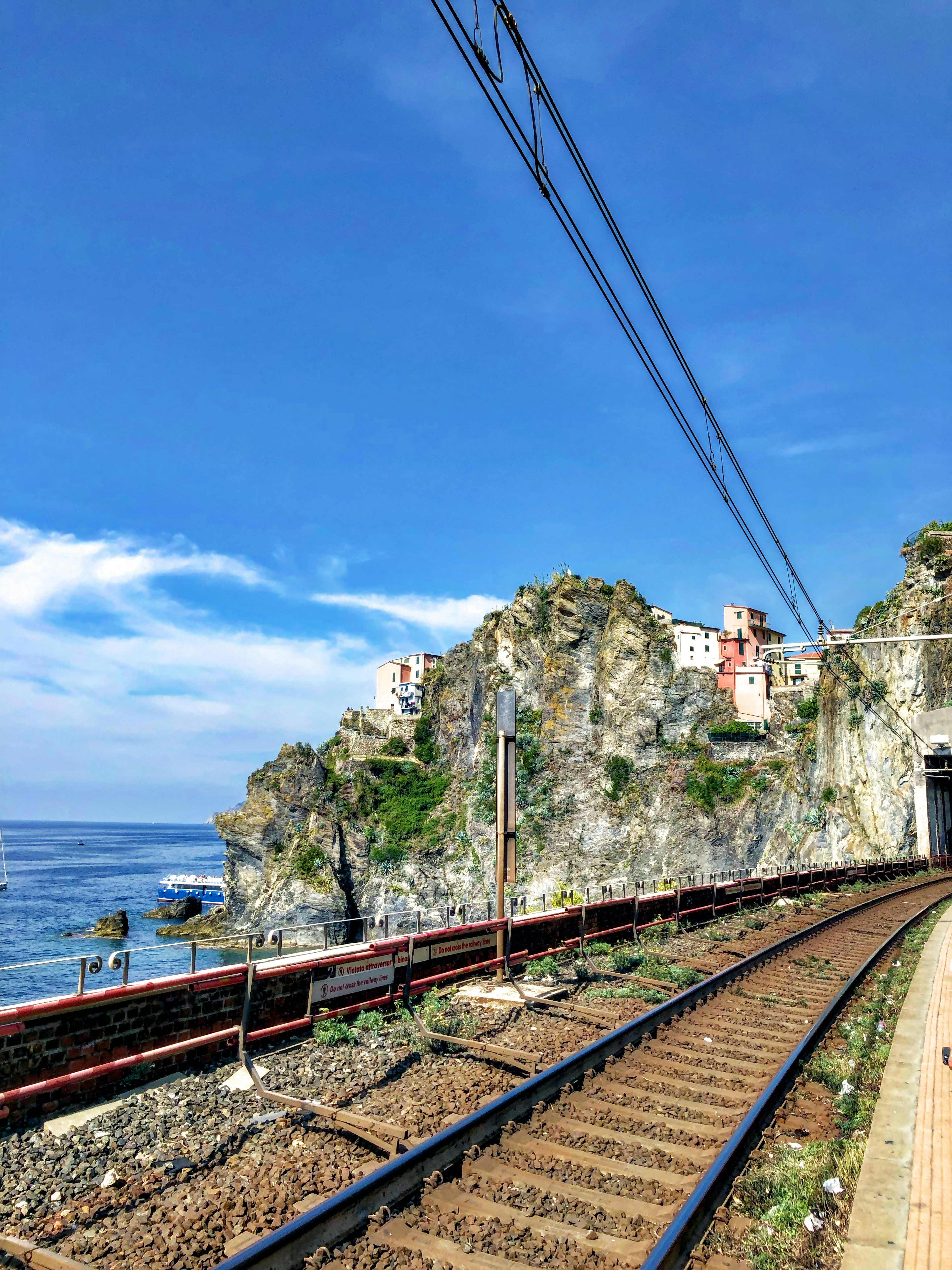 Vía de tren costera a lo largo de un acantilado con cielo azul y nubes blancas