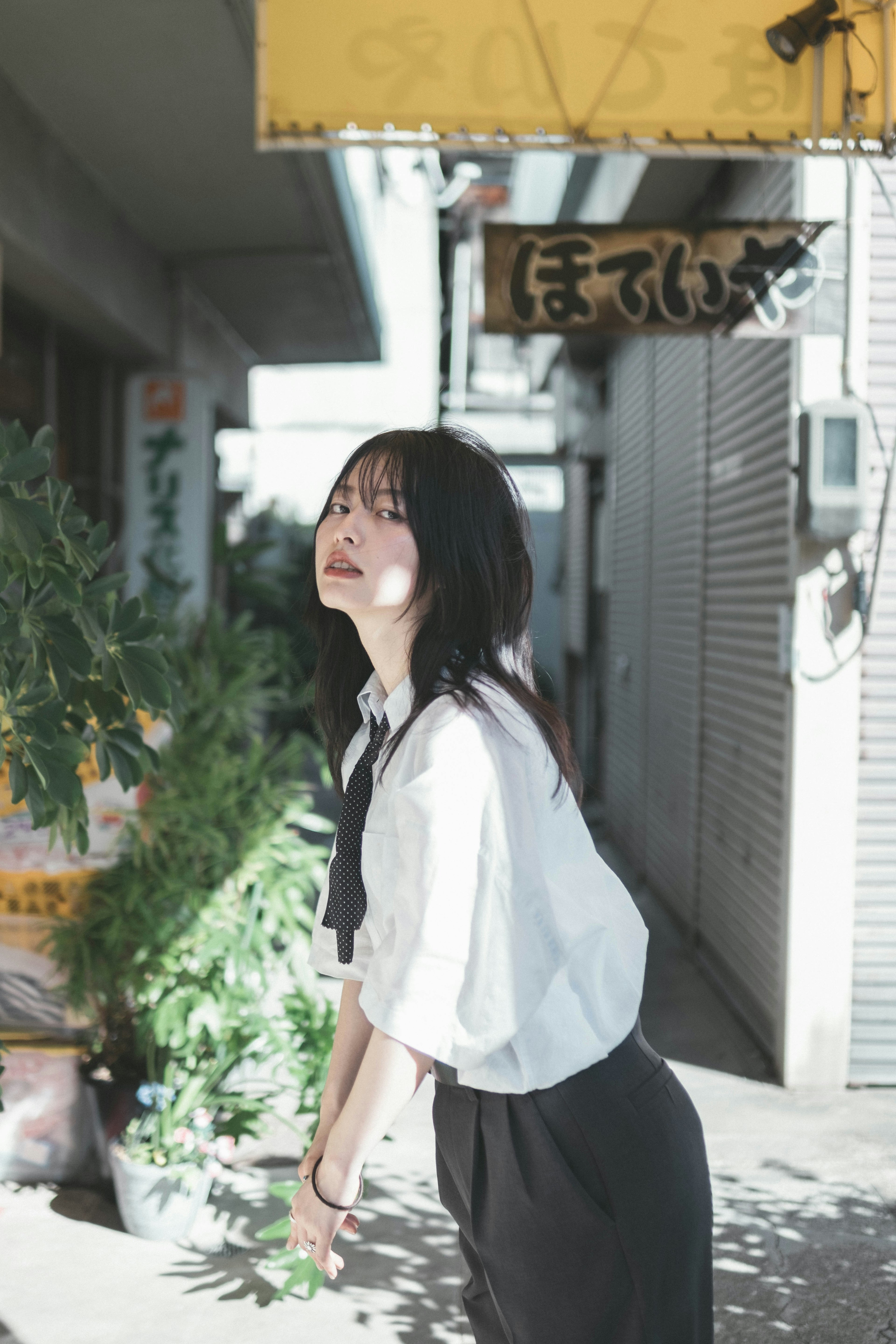 A woman smiling in the street wearing a white shirt and black skirt with plants nearby