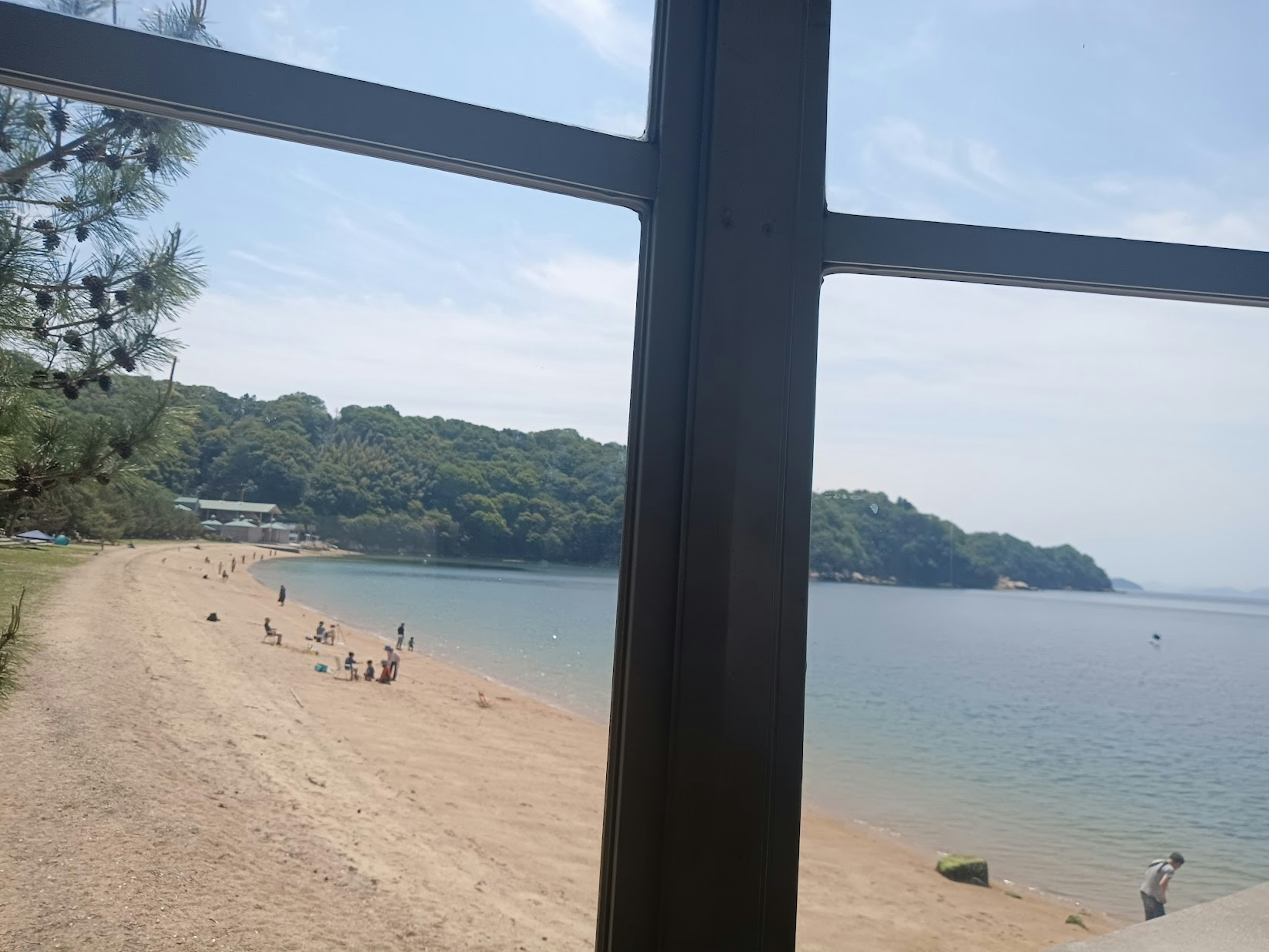 Vista de una playa y el mar a través de una ventana Personas en la arena con vegetación al fondo