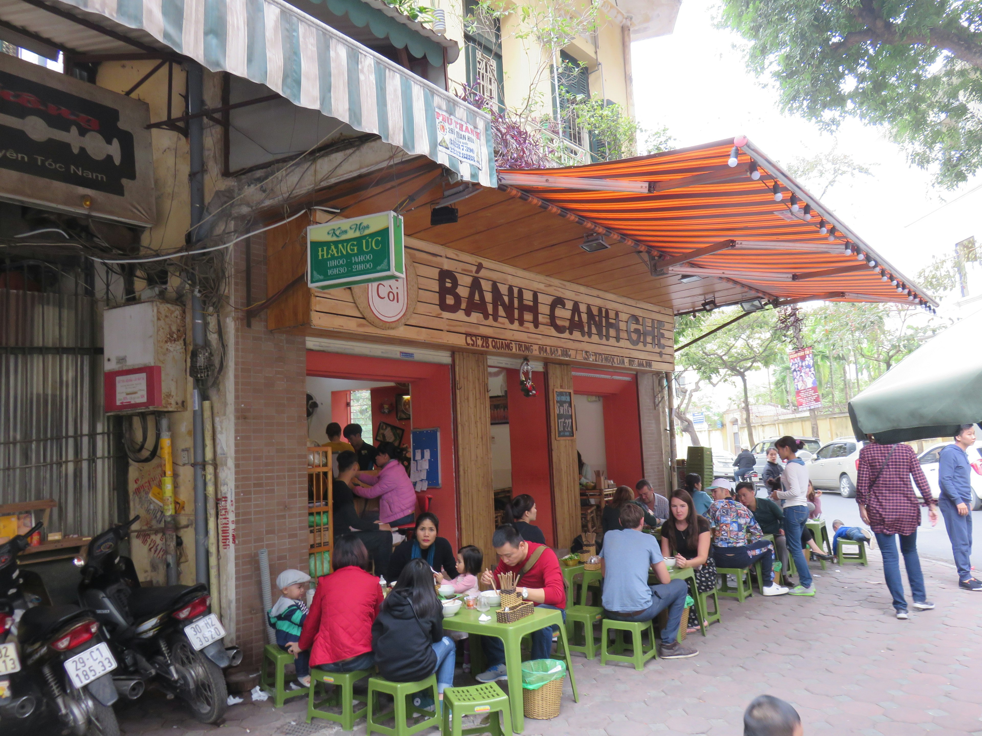 Exterior of a Vietnamese Bánh Căn restaurant with patrons enjoying meals