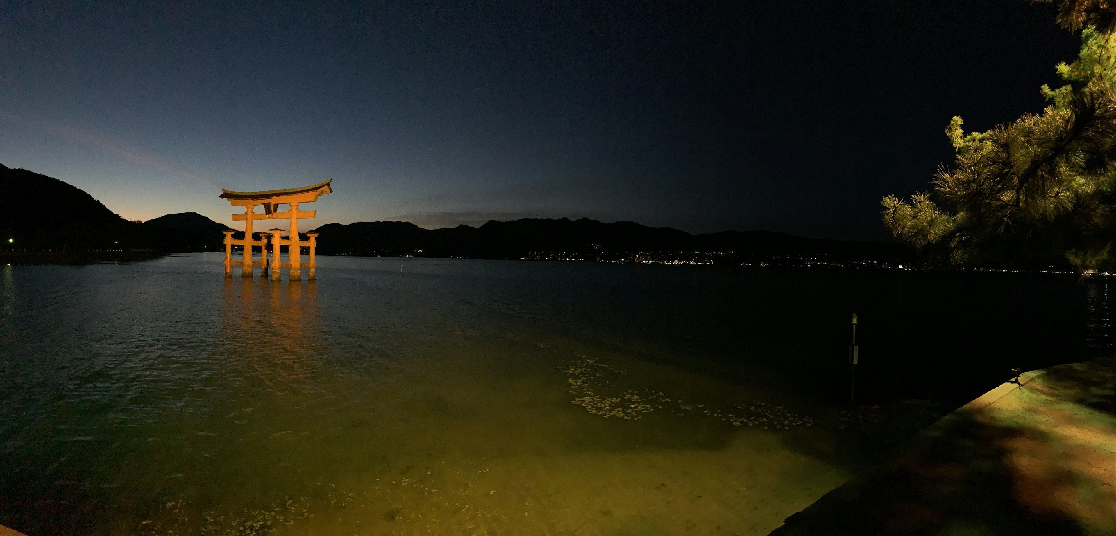 Vista nocturna del torii en el Santuario de Itsukushima en Miyajima con aguas tranquilas