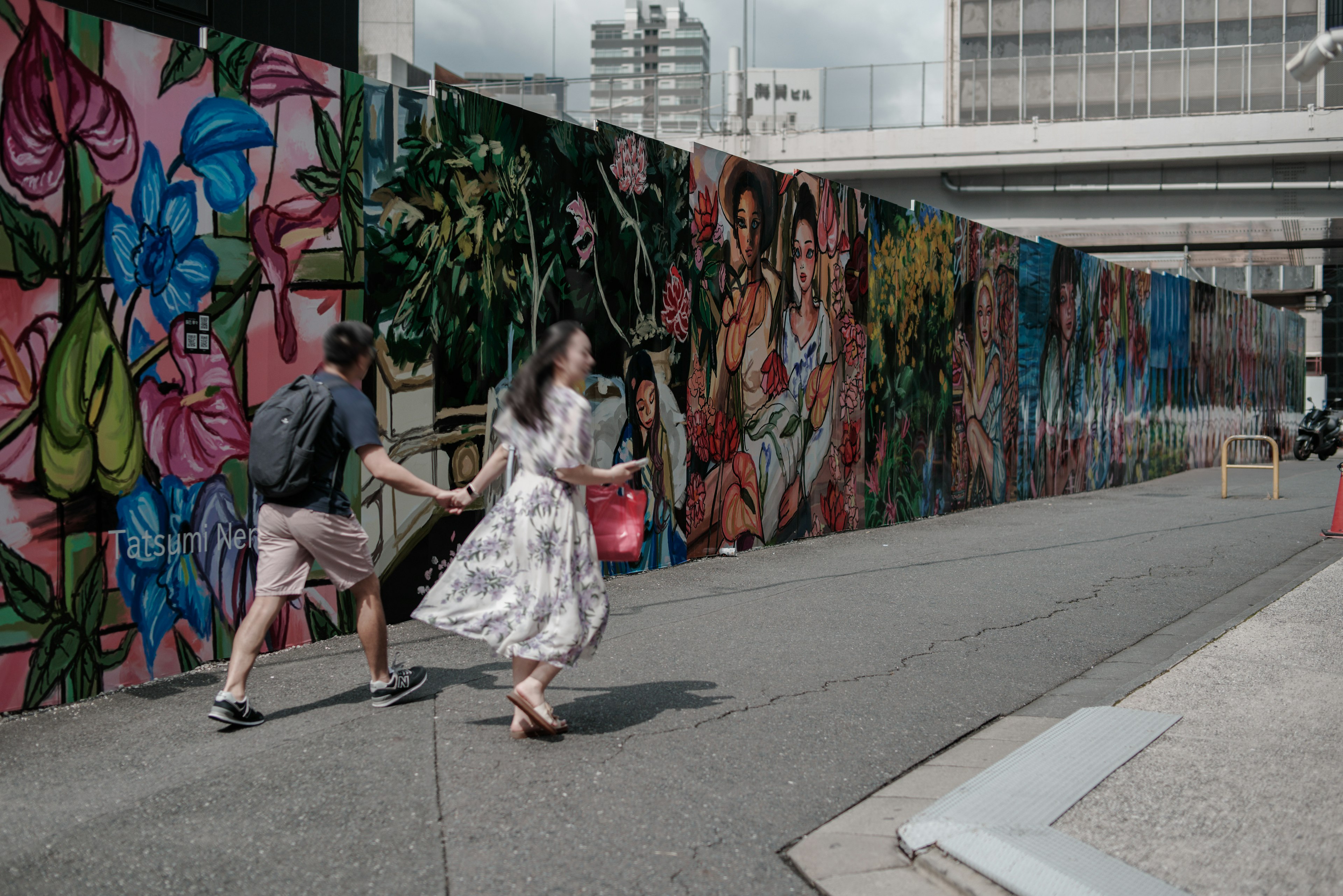 Coppia che cammina davanti a un murale vibrante con fiori e foglie