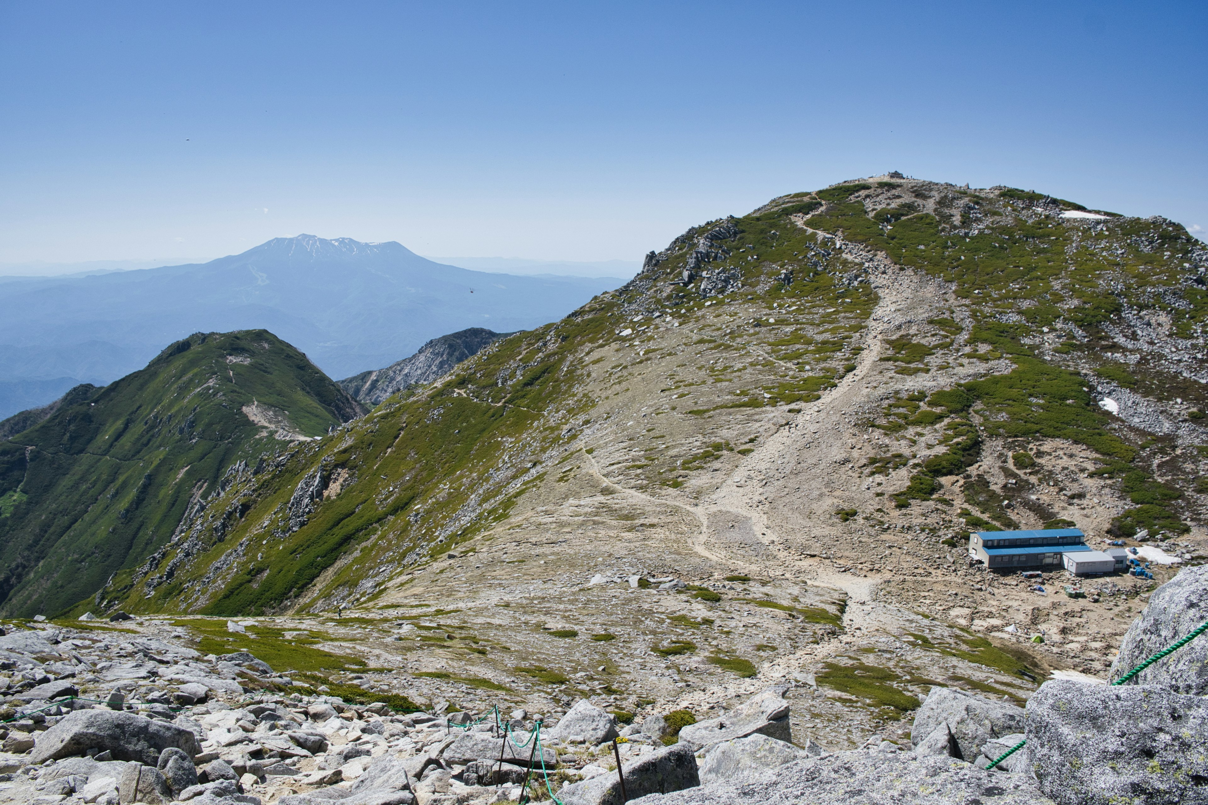 Paysage de montagne avec des collines vertes et un petit bâtiment sous un ciel bleu