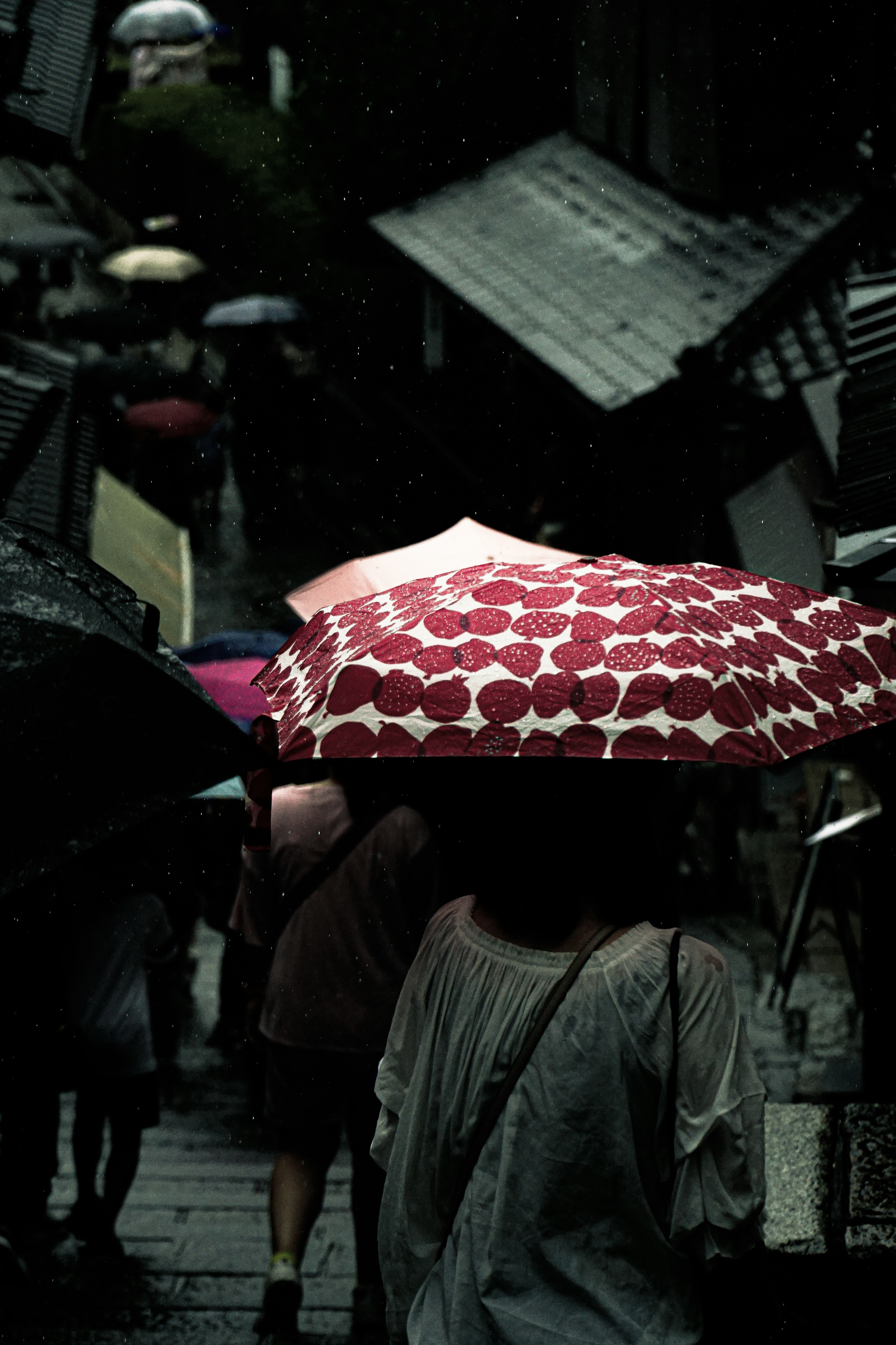 人們在雨中走，撐著紅色心形圖案的傘的場景