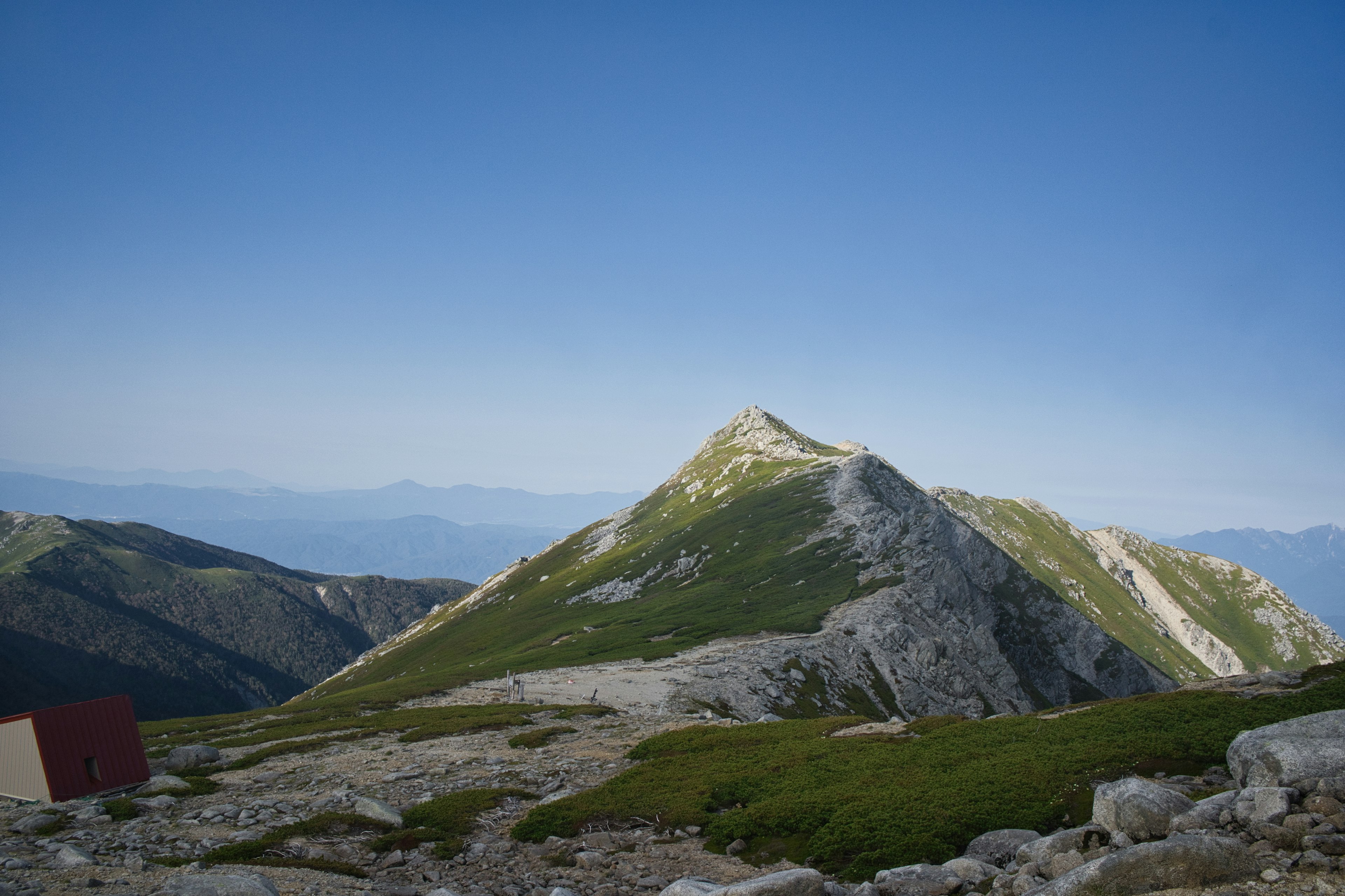 Vue panoramique d'un sommet de montagne avec de la végétation verte et un ciel bleu clair