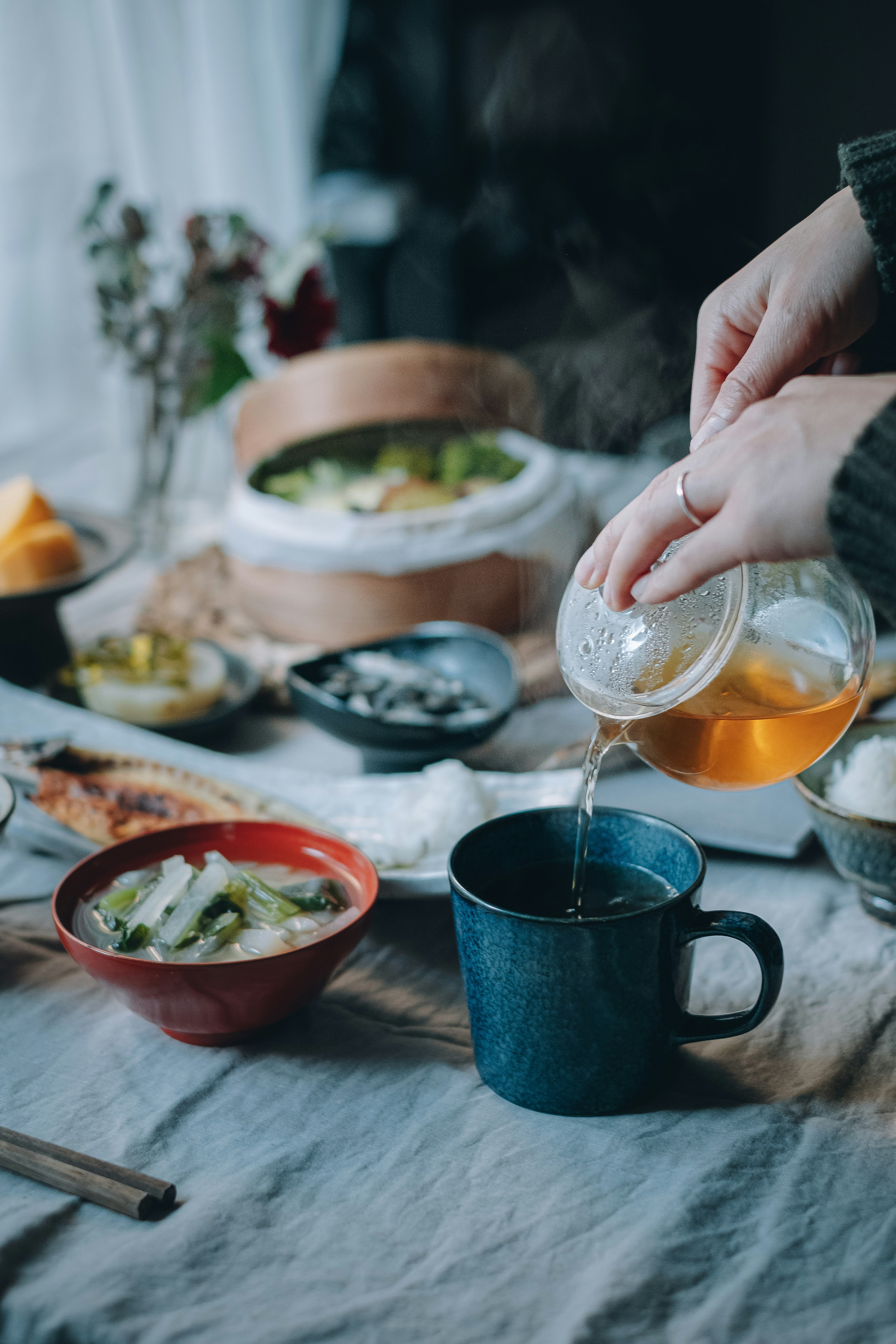 手将茶倒入蓝色杯中，桌上摆放着各种菜肴