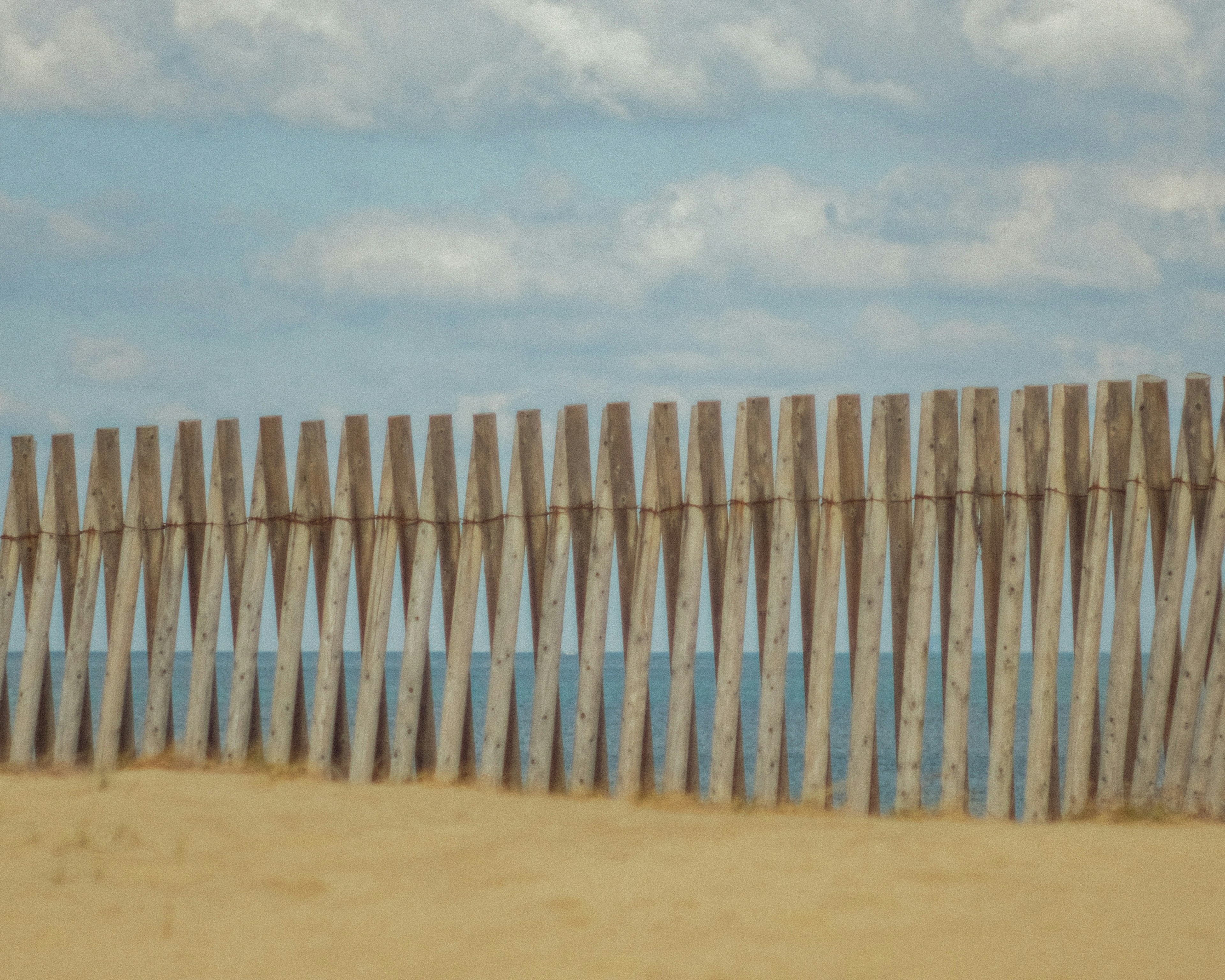 Wooden fence on sandy beach with blue ocean and sky