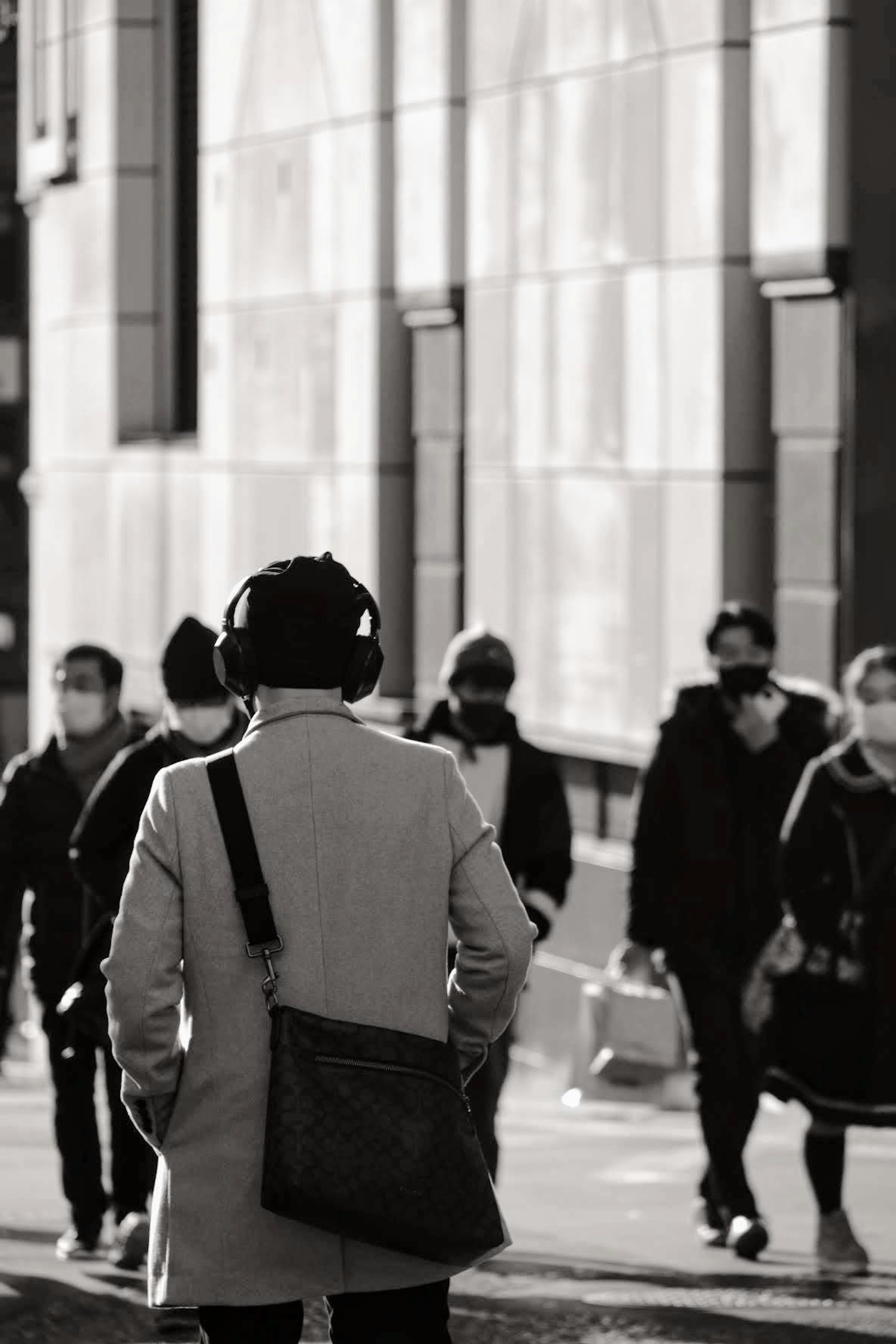 Scène urbaine en noir et blanc avec des personnes marchant Un homme avec des écouteurs vu de dos