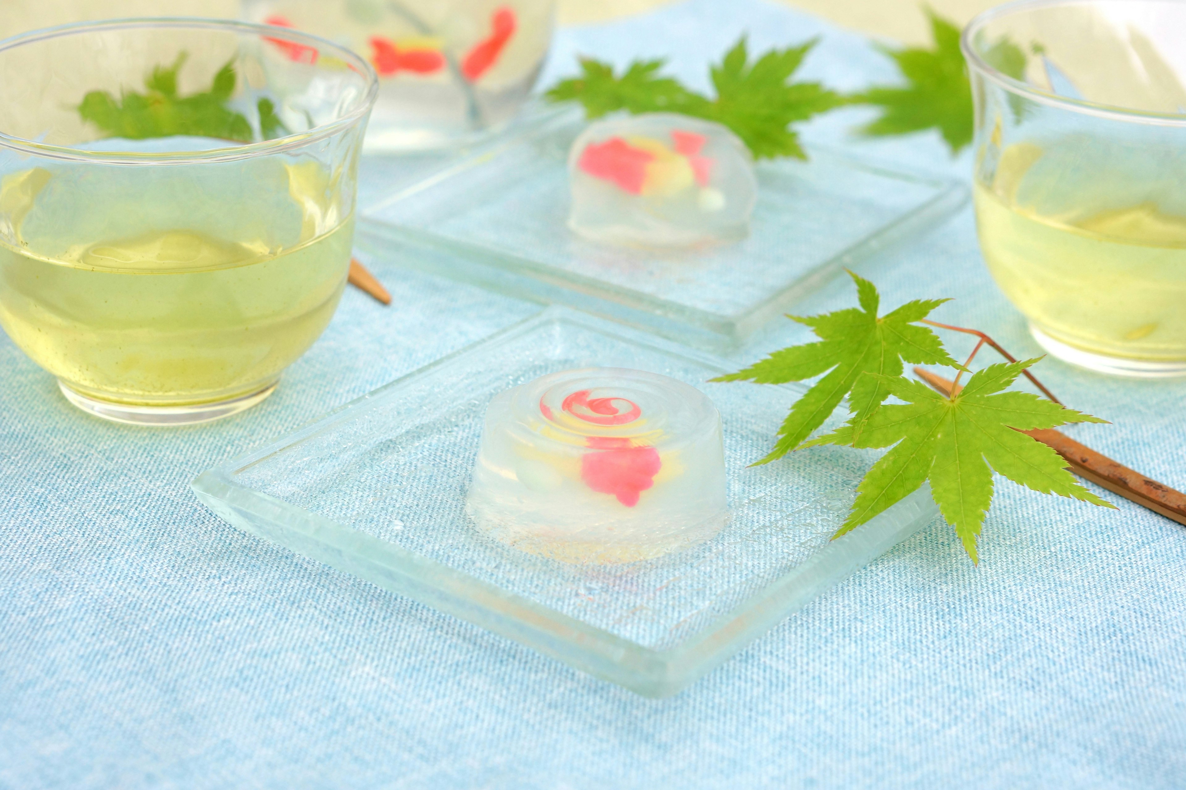 Dulces japoneses transparentes con flores rosas y hojas verdes sobre una mesa azul