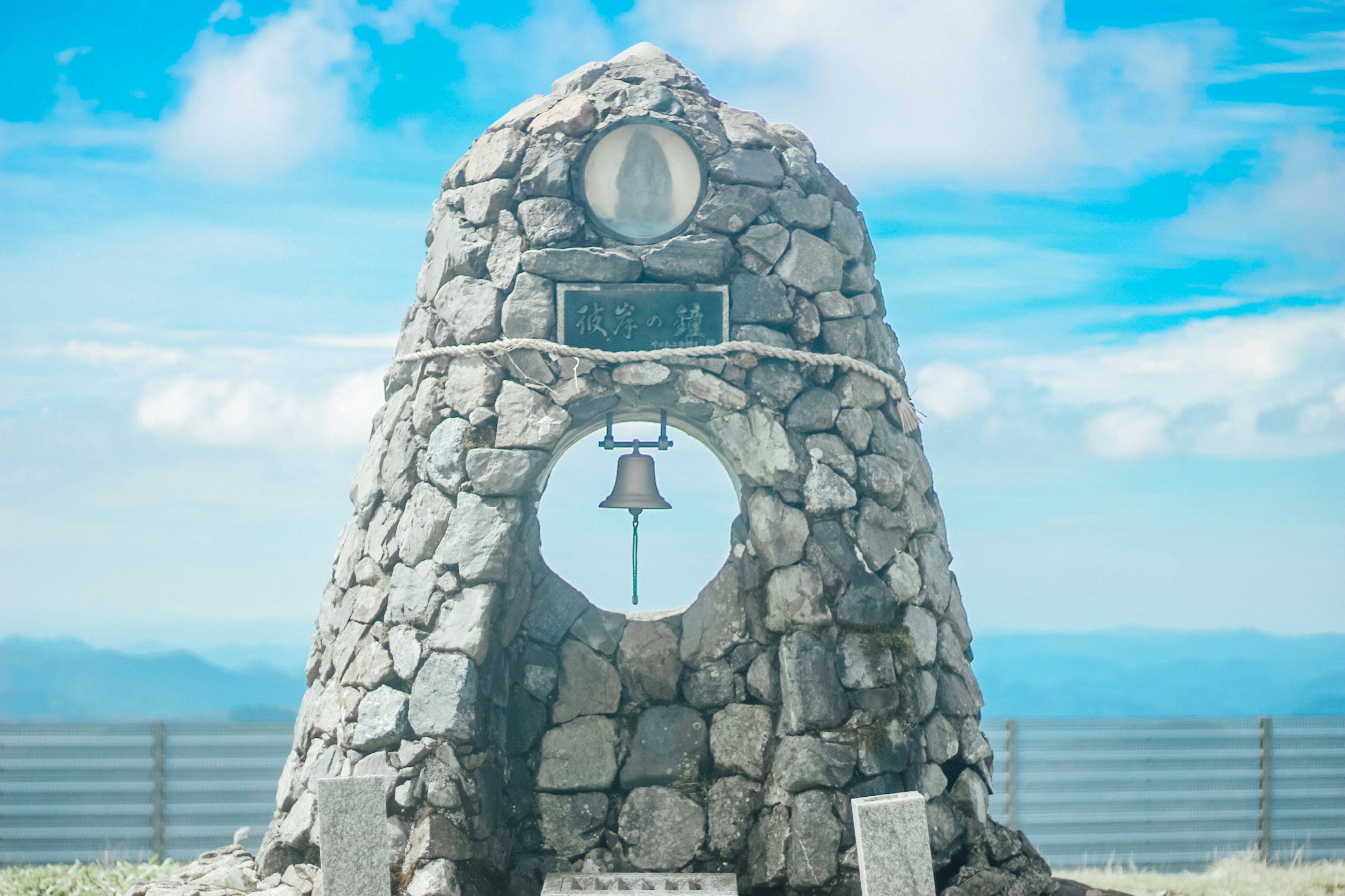 Monumen batu dengan lonceng di bawah langit biru