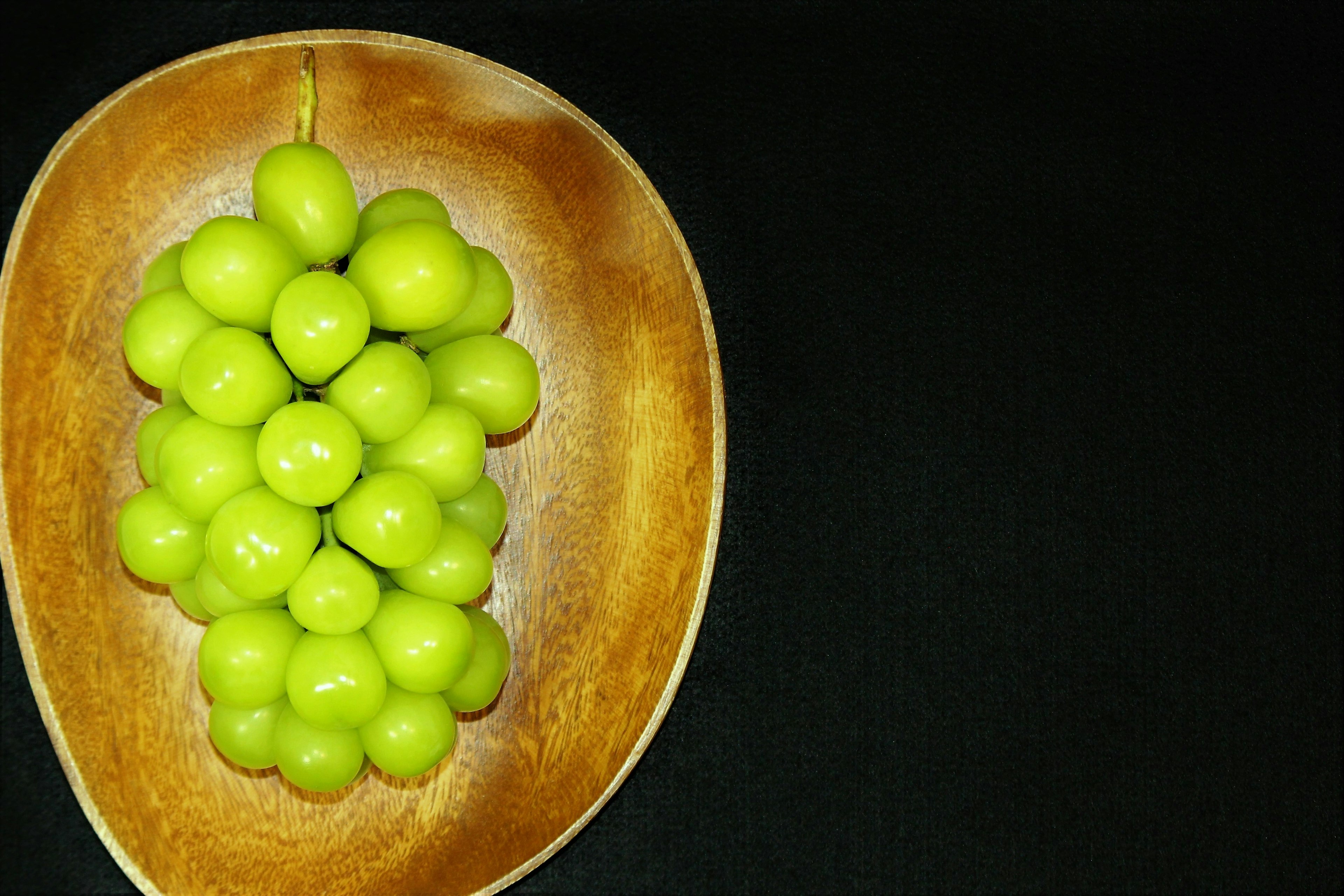 Un grappolo di uva verde in una ciotola di legno su sfondo nero