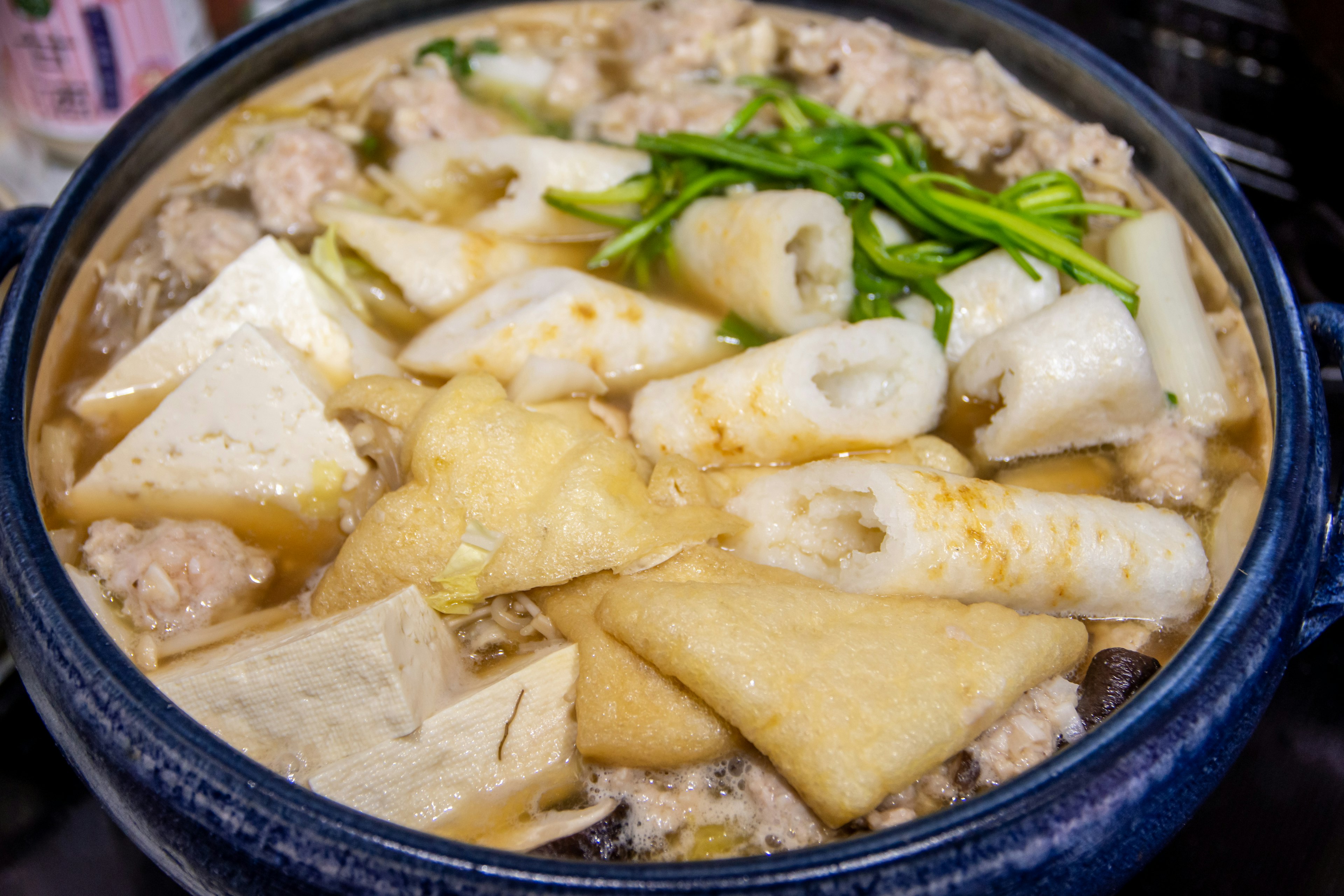 A hot pot filled with meatballs, tofu, green onions, and various ingredients