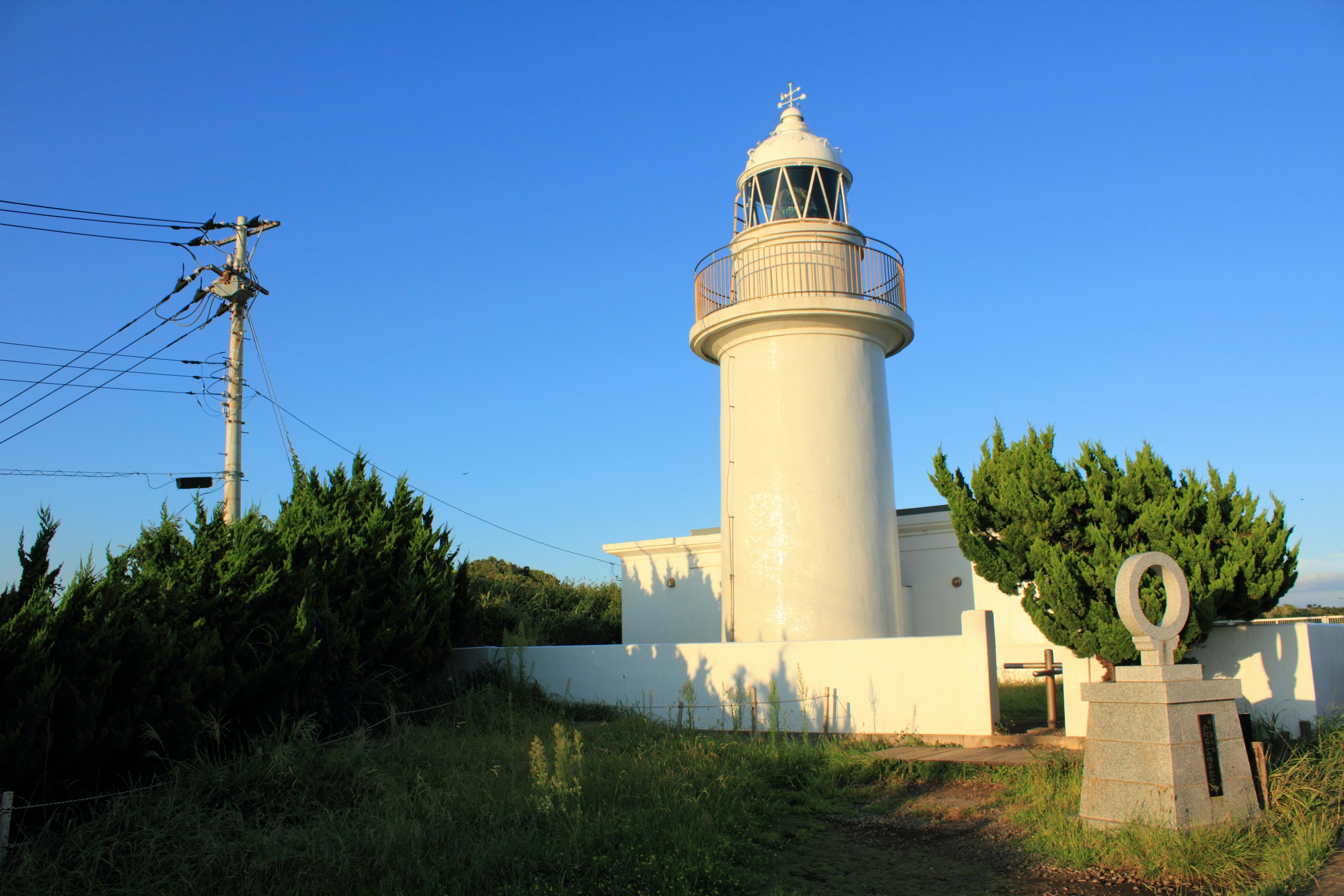 Phare blanc sous un ciel bleu avec des plantes vertes