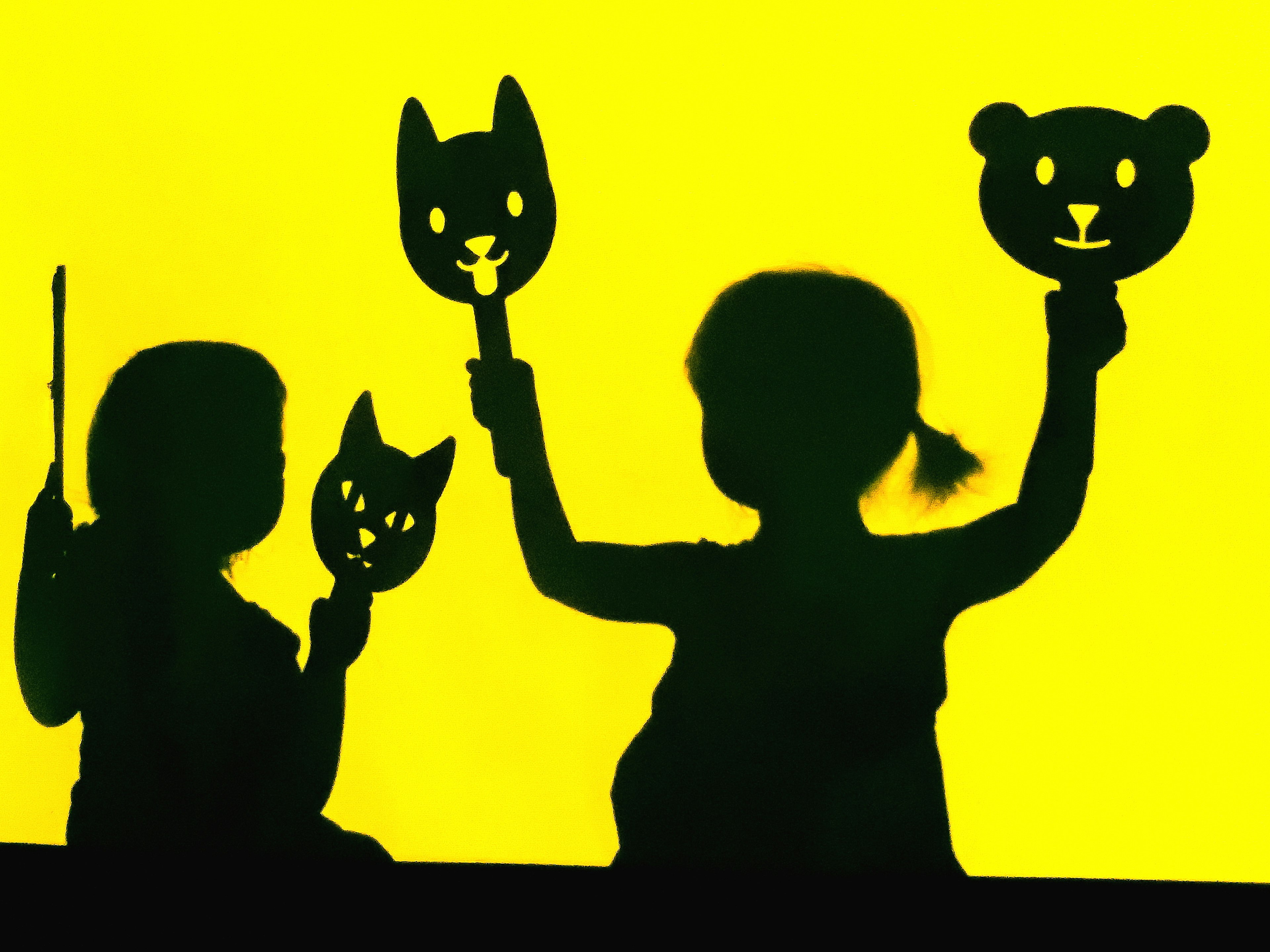 Silhouettes of children holding animal masks against a yellow background