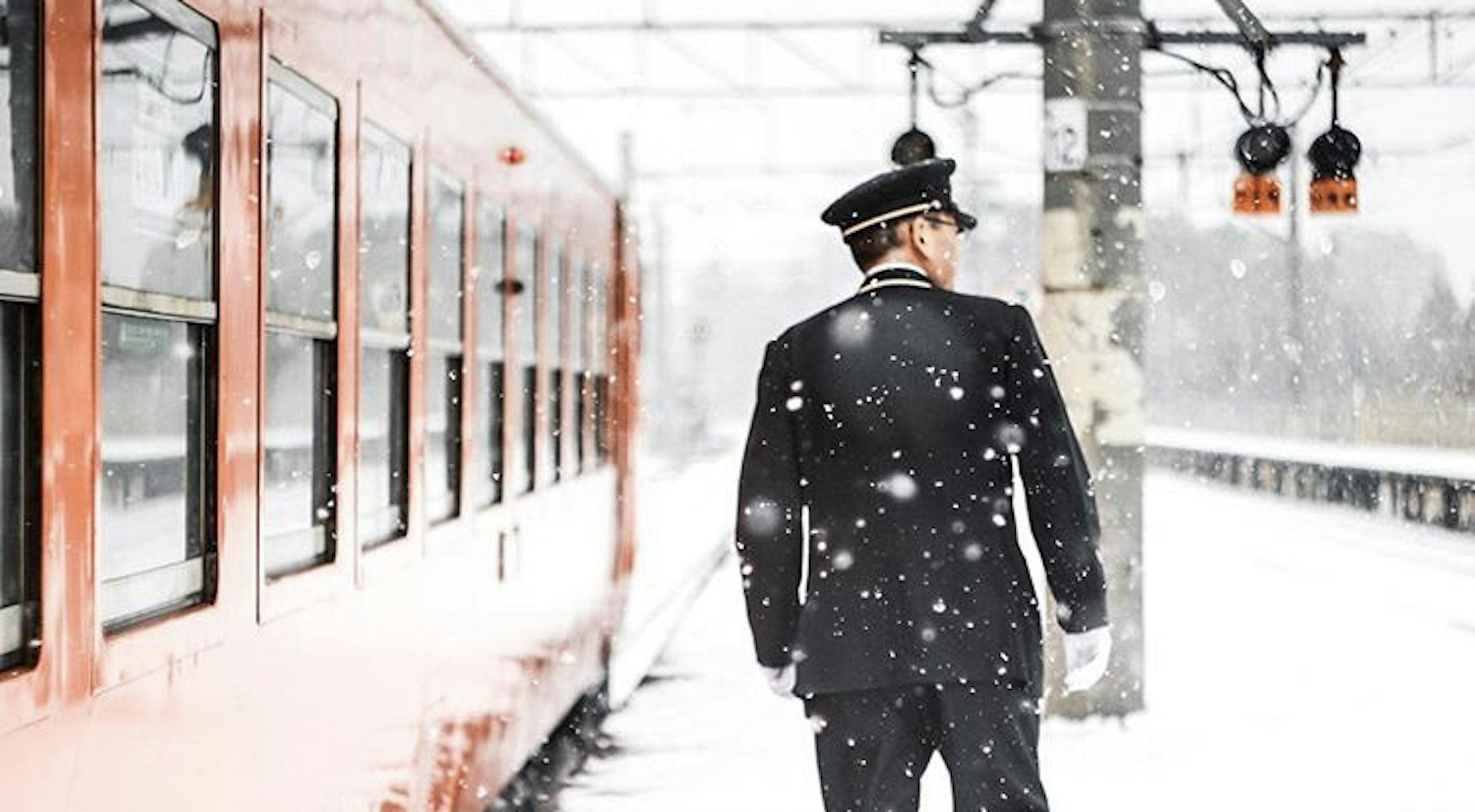 雪の中で列車を見守る駅員の後姿