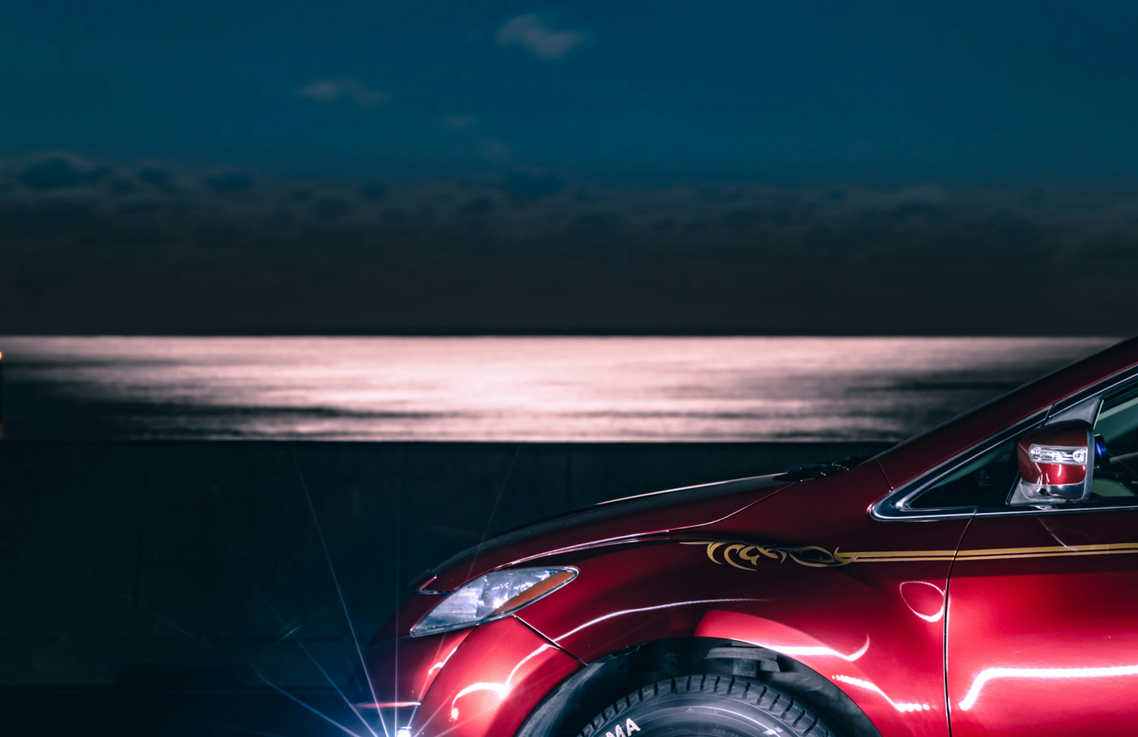 Side view of a red car with ocean backdrop at night