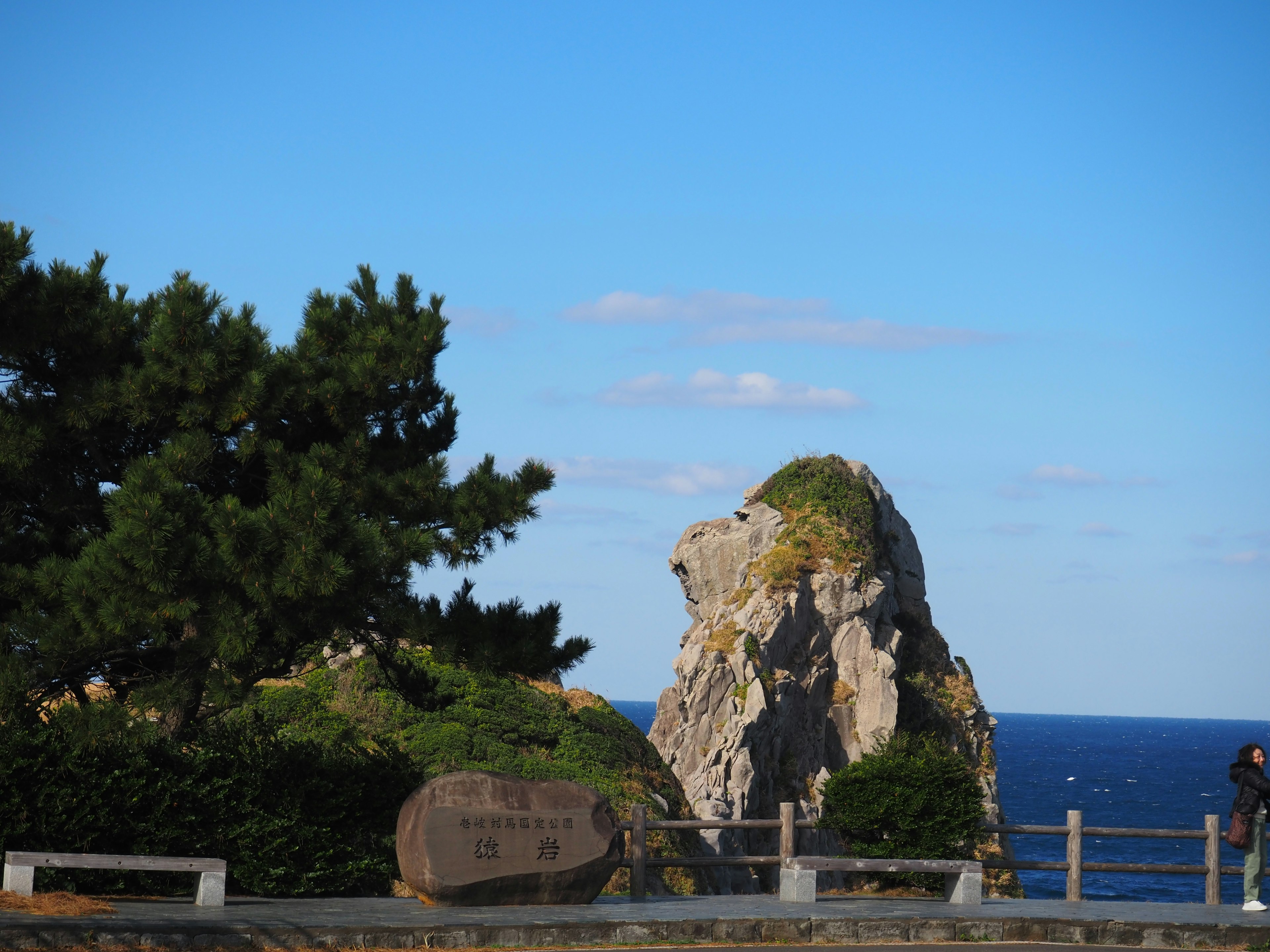 Large rock against a backdrop of blue sea and sky with green trees