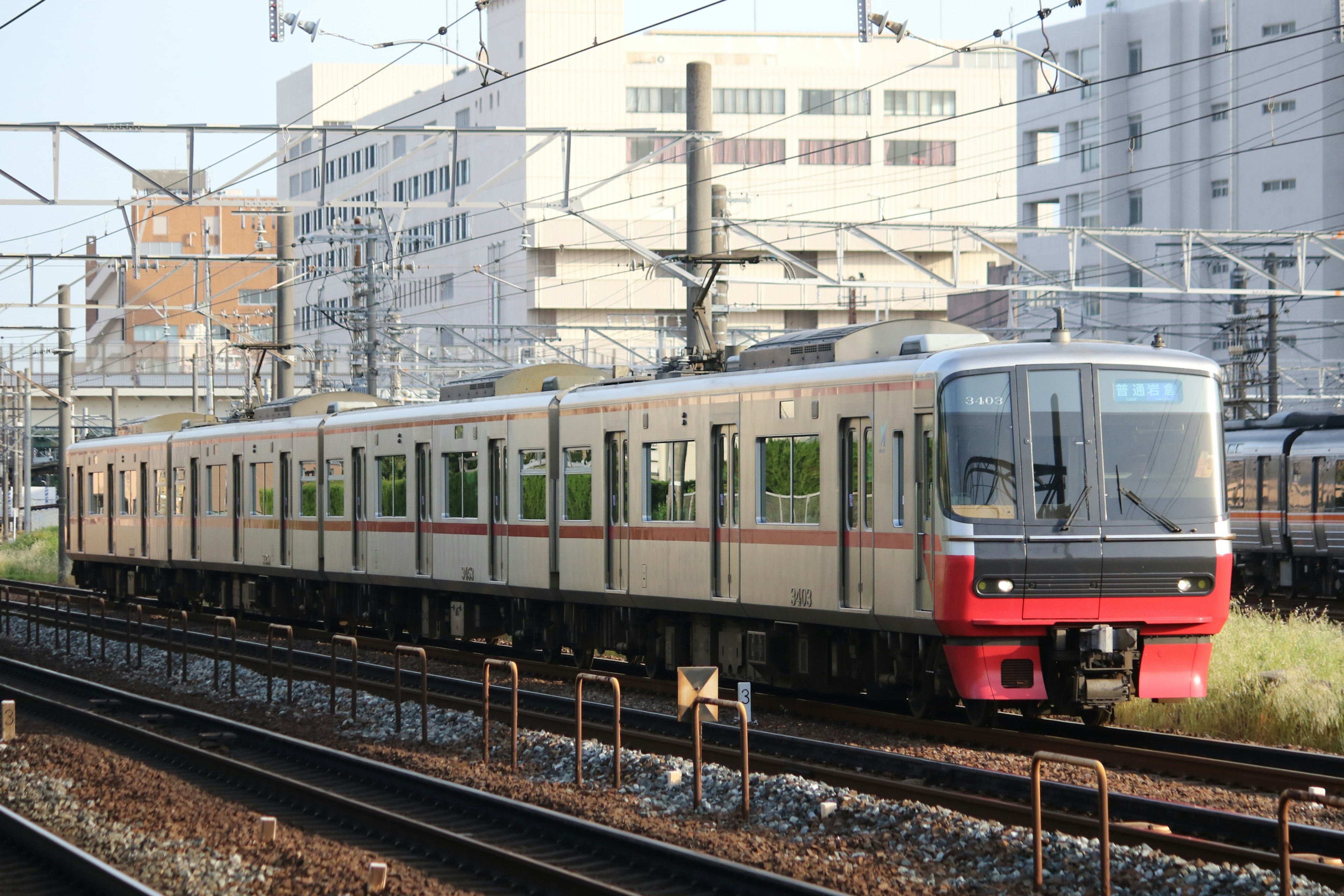 A commuter train with a red front is running on tracks with buildings in the background