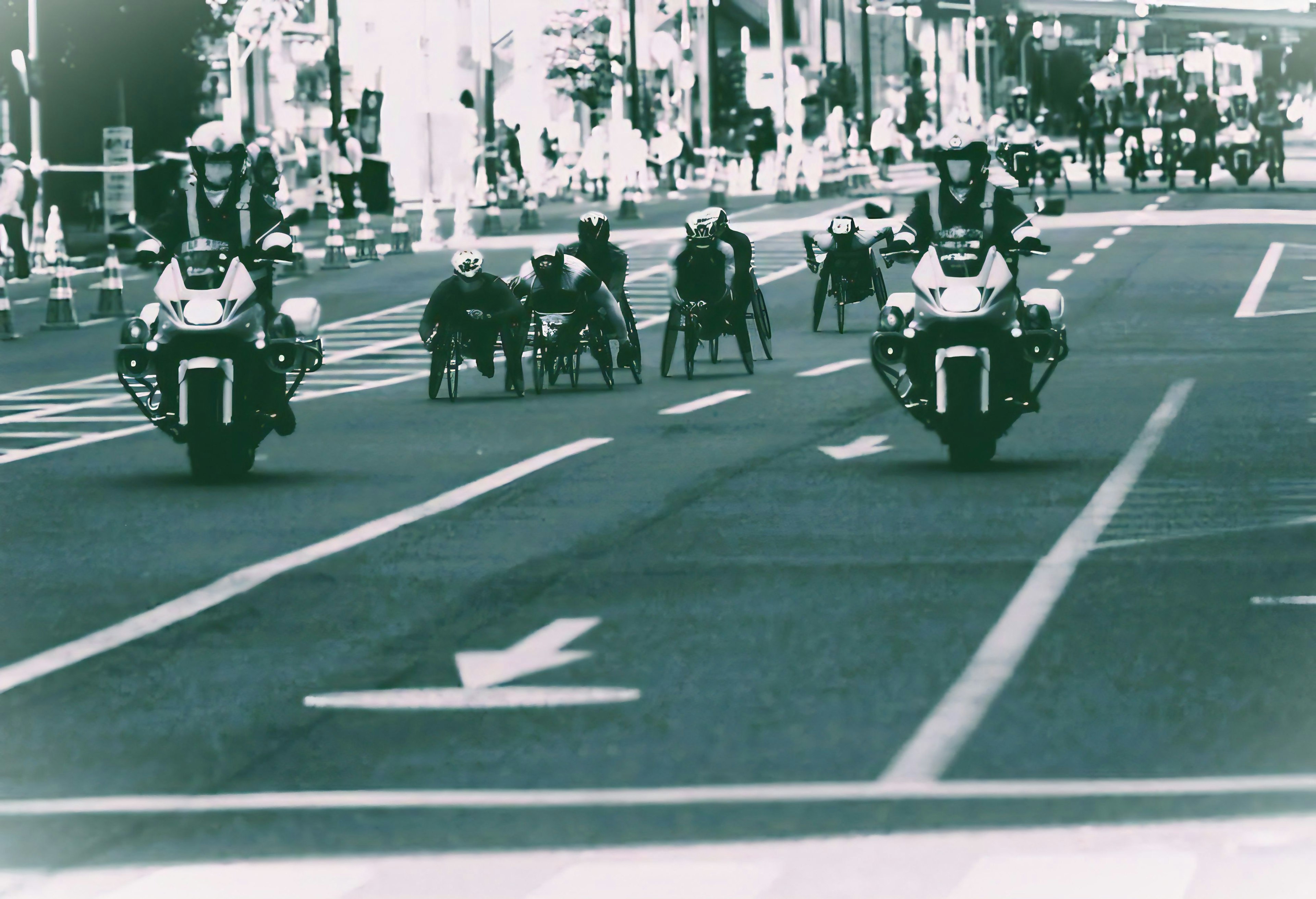 Schwarzweißfoto von Polizeibeamten auf Motorrädern, die eine Gruppe von Rollstuhlsportlern auf der Straße anführen