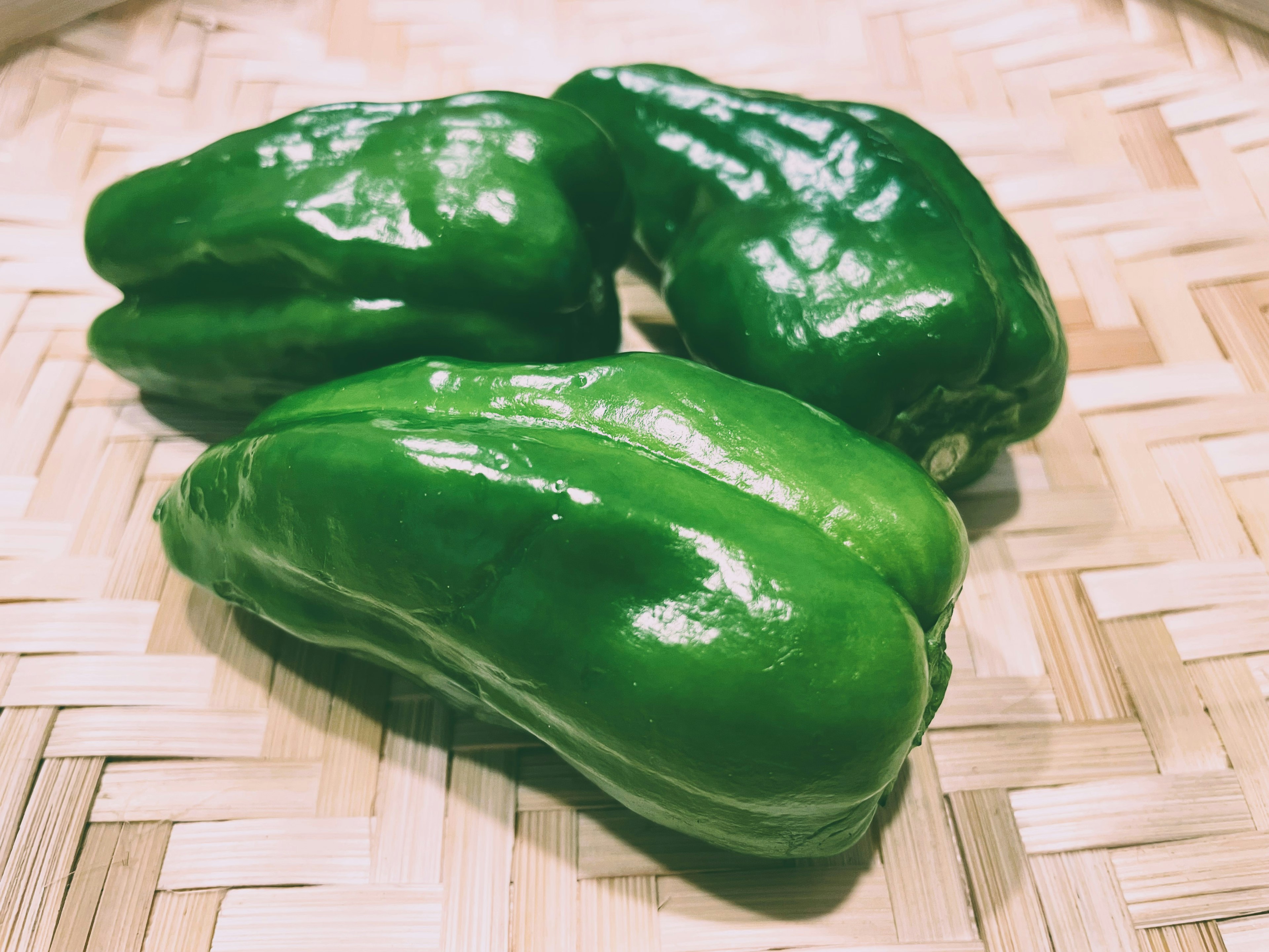 Three vibrant green peppers placed on a woven bamboo mat