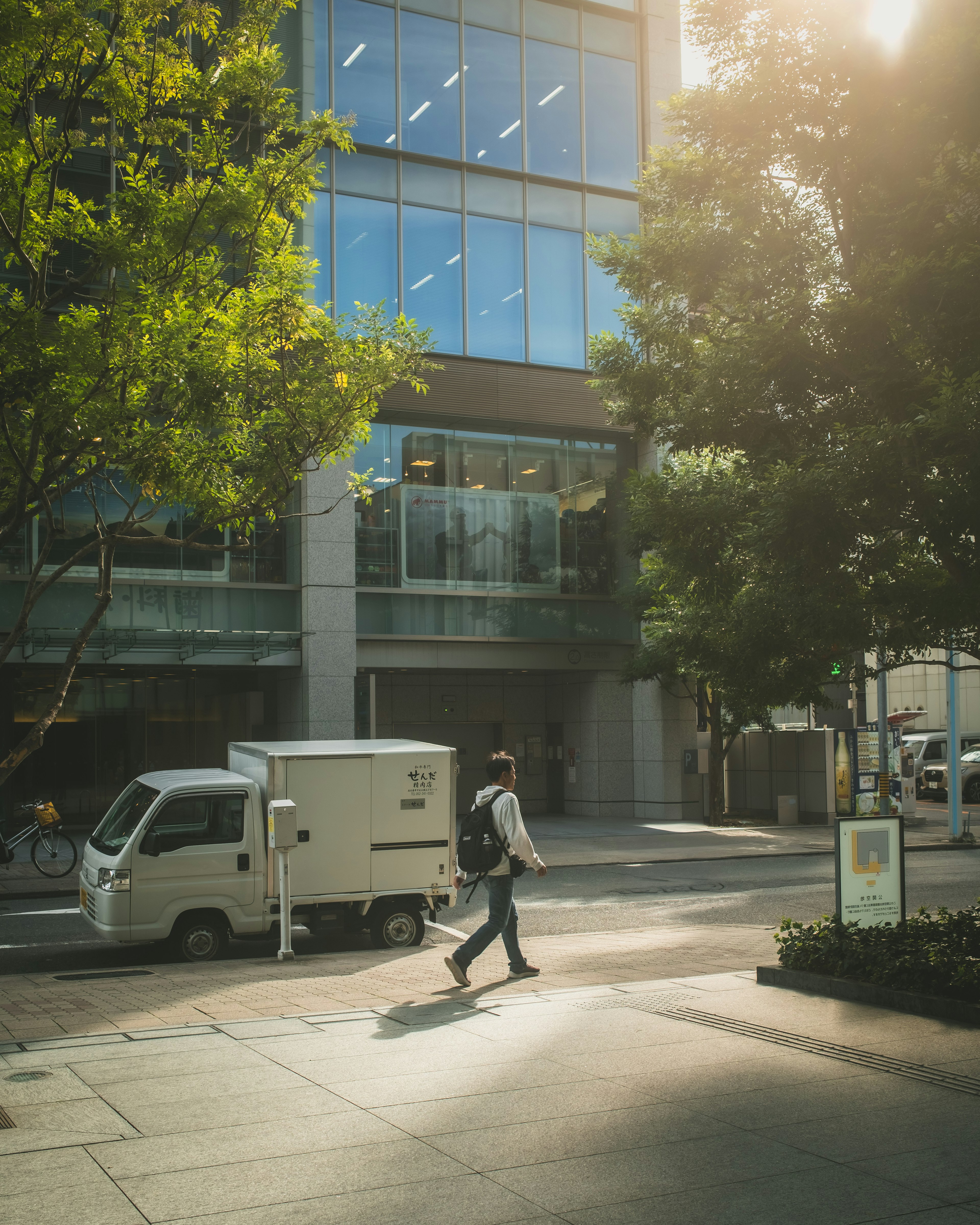 A person walking on an urban street in front of a commercial building with a parked small truck