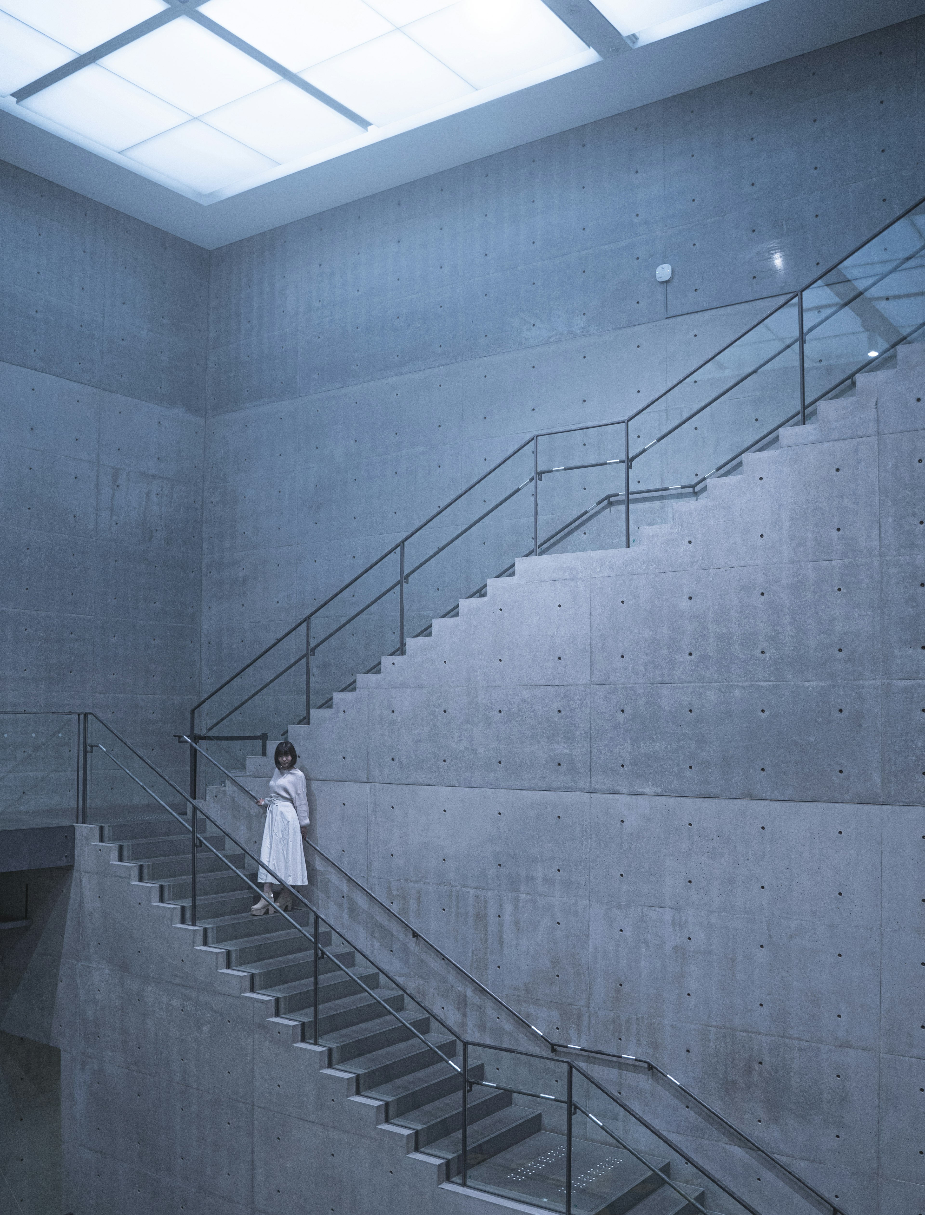 A woman in a white dress ascending a modern staircase with blue tones