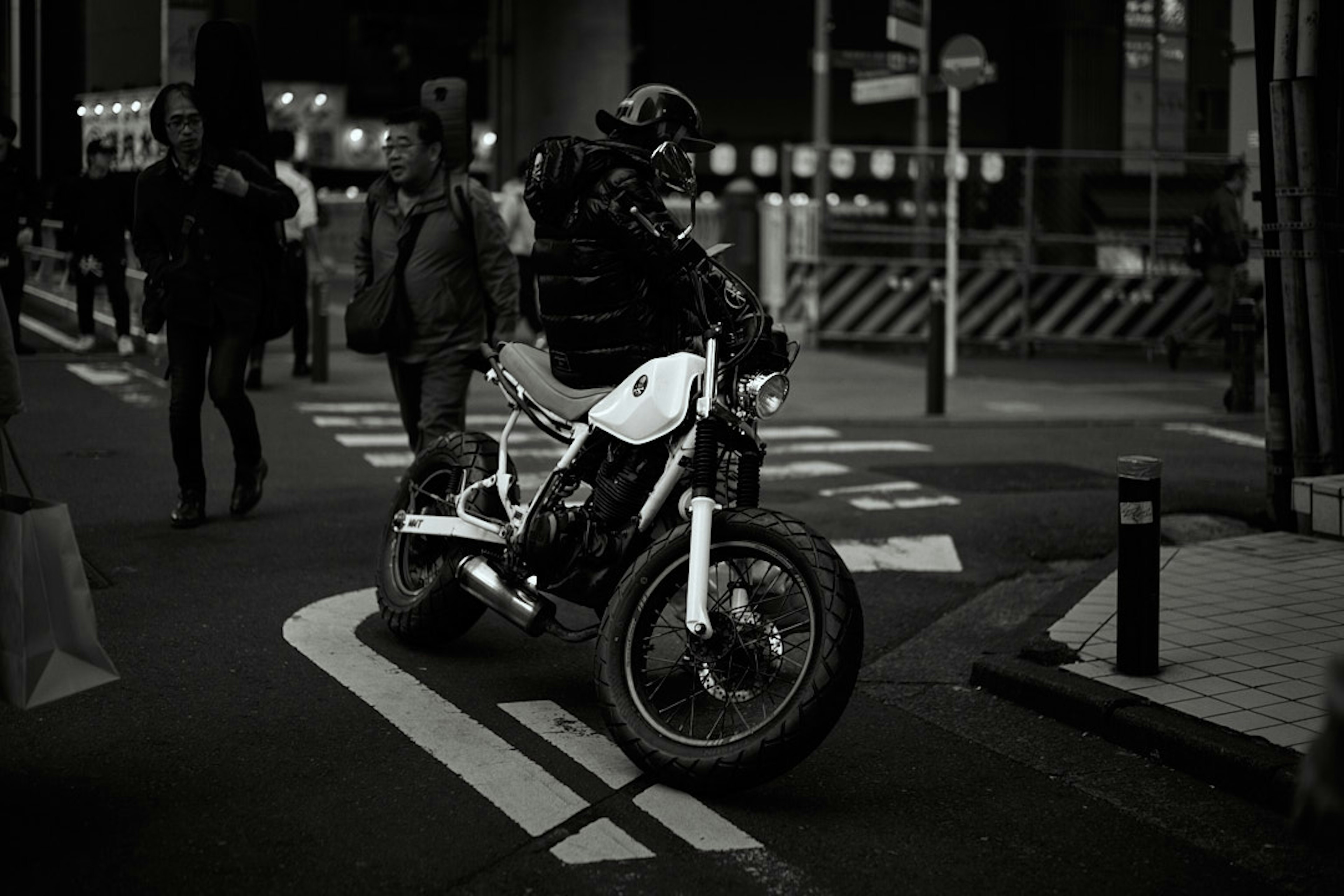 Eine schwarz-weiße Straßenszene mit einem Motorrad und Fußgängern