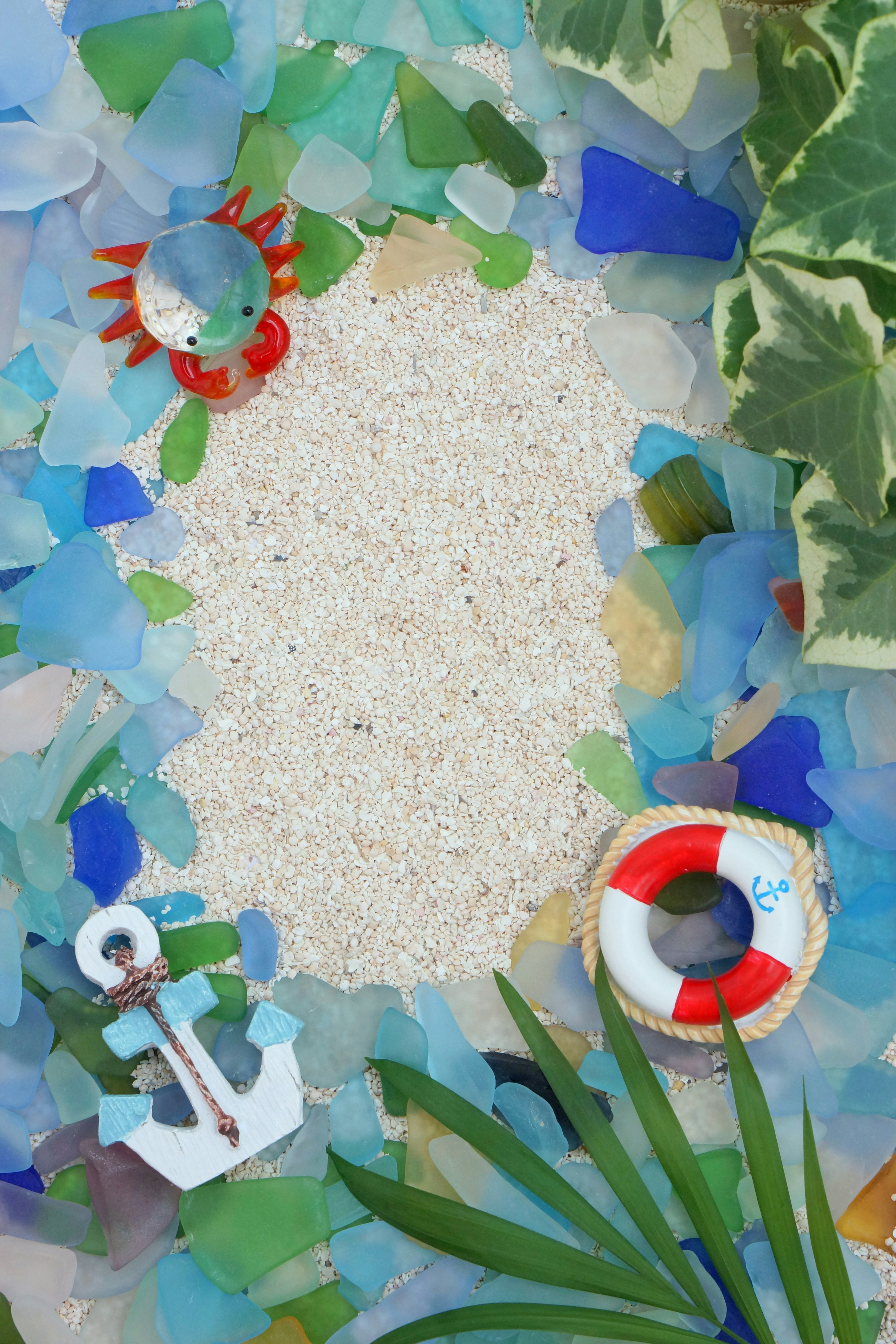 Colorful sea glass and sand background featuring a red crab and a life preserver