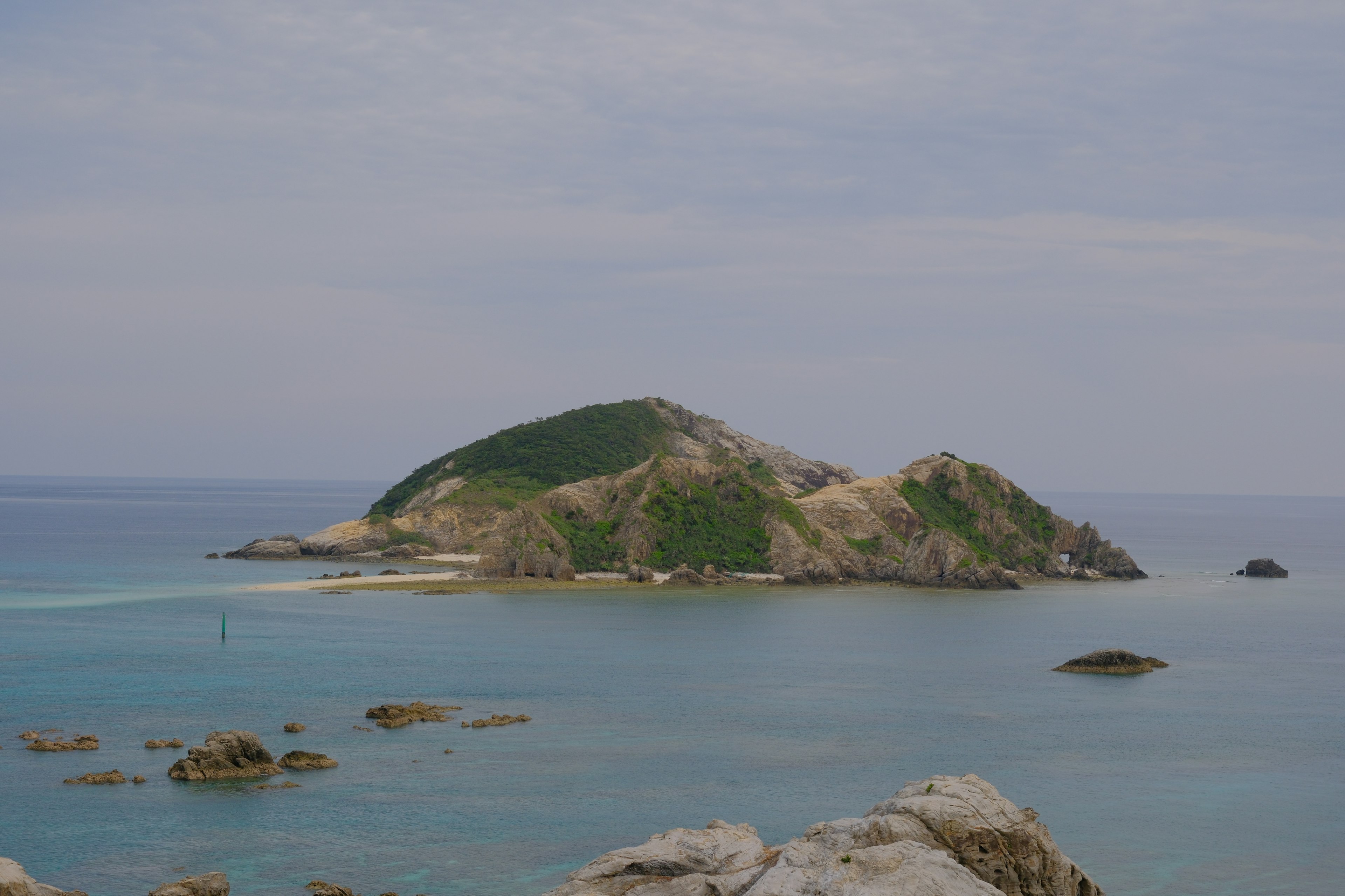 Eine grüne Insel umgeben von blauem Meer und felsigen Küsten